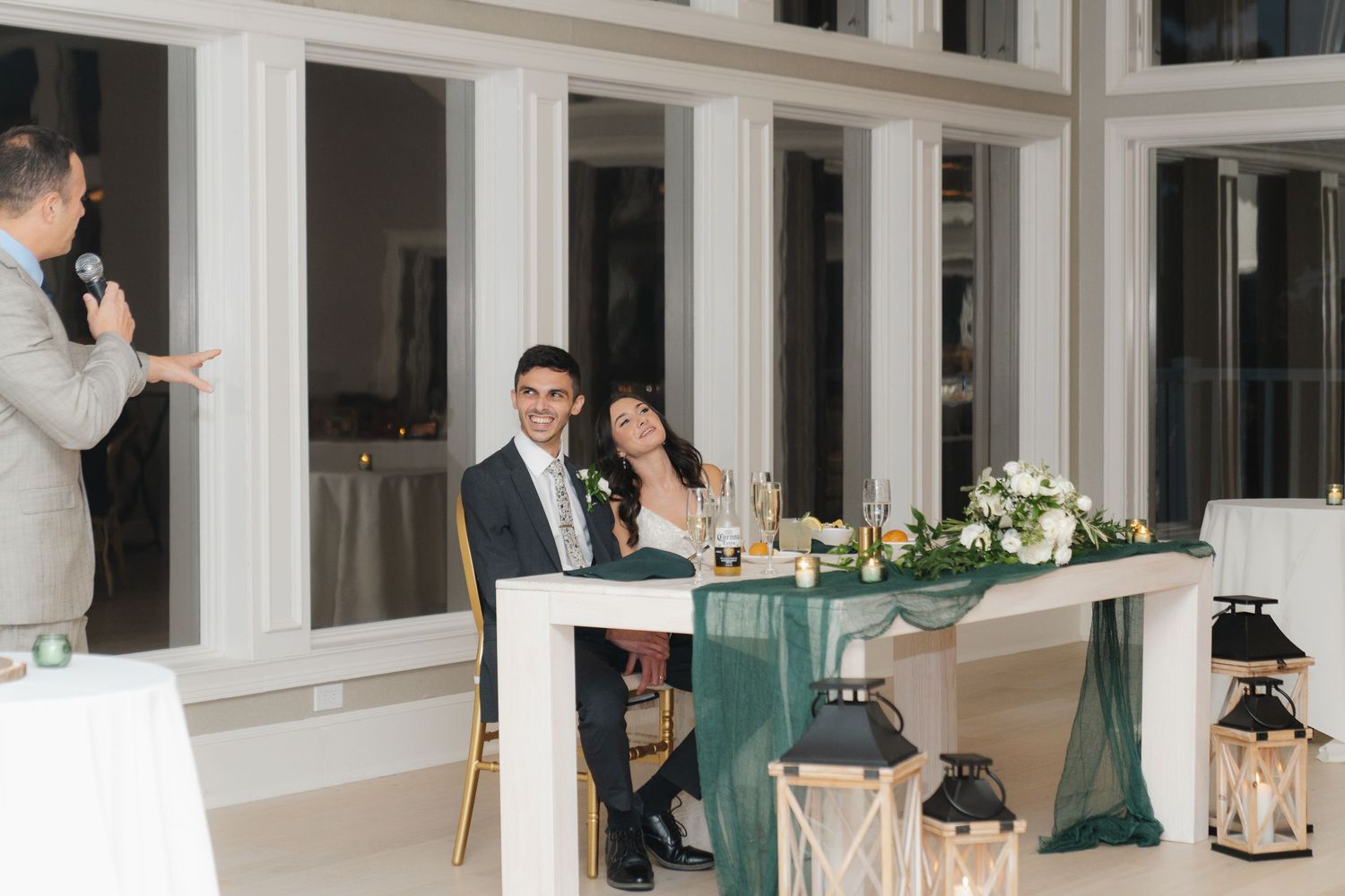 Elegant wedding reception venue with white columns, green tablecloths and romantic candlelight decor.