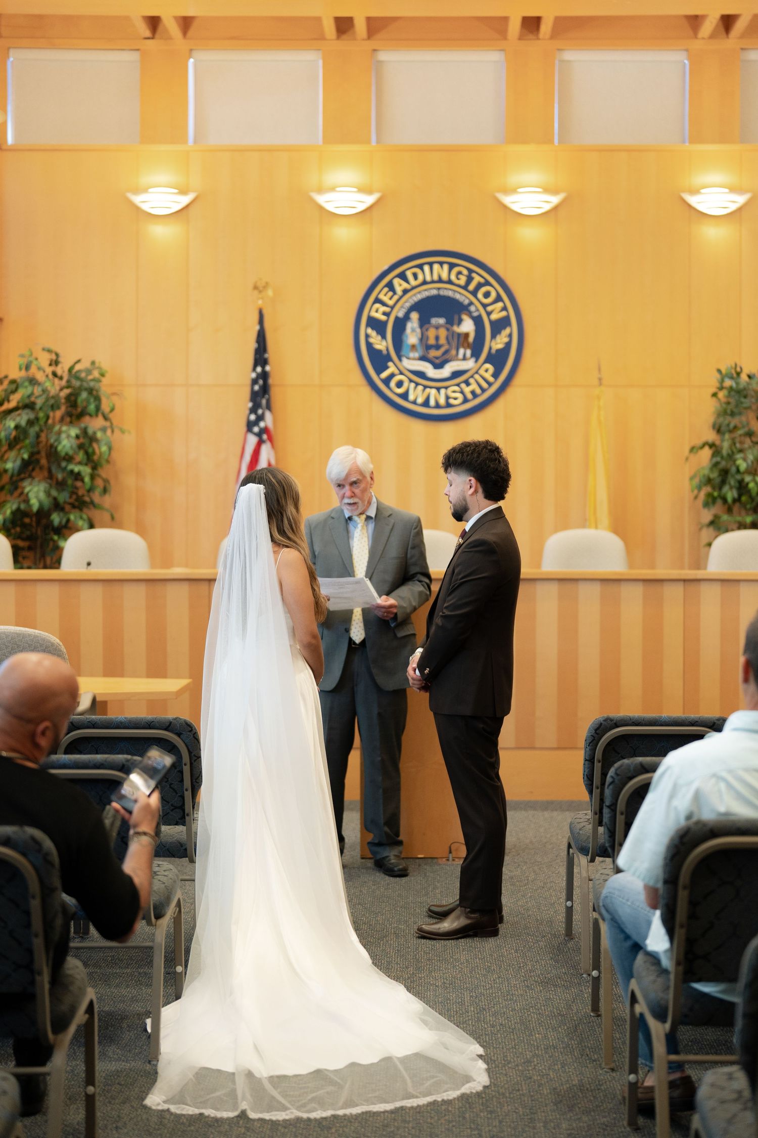 Couple exchanging vows at Readington Township courthouse civil wedding ceremony with officiant and American flag.