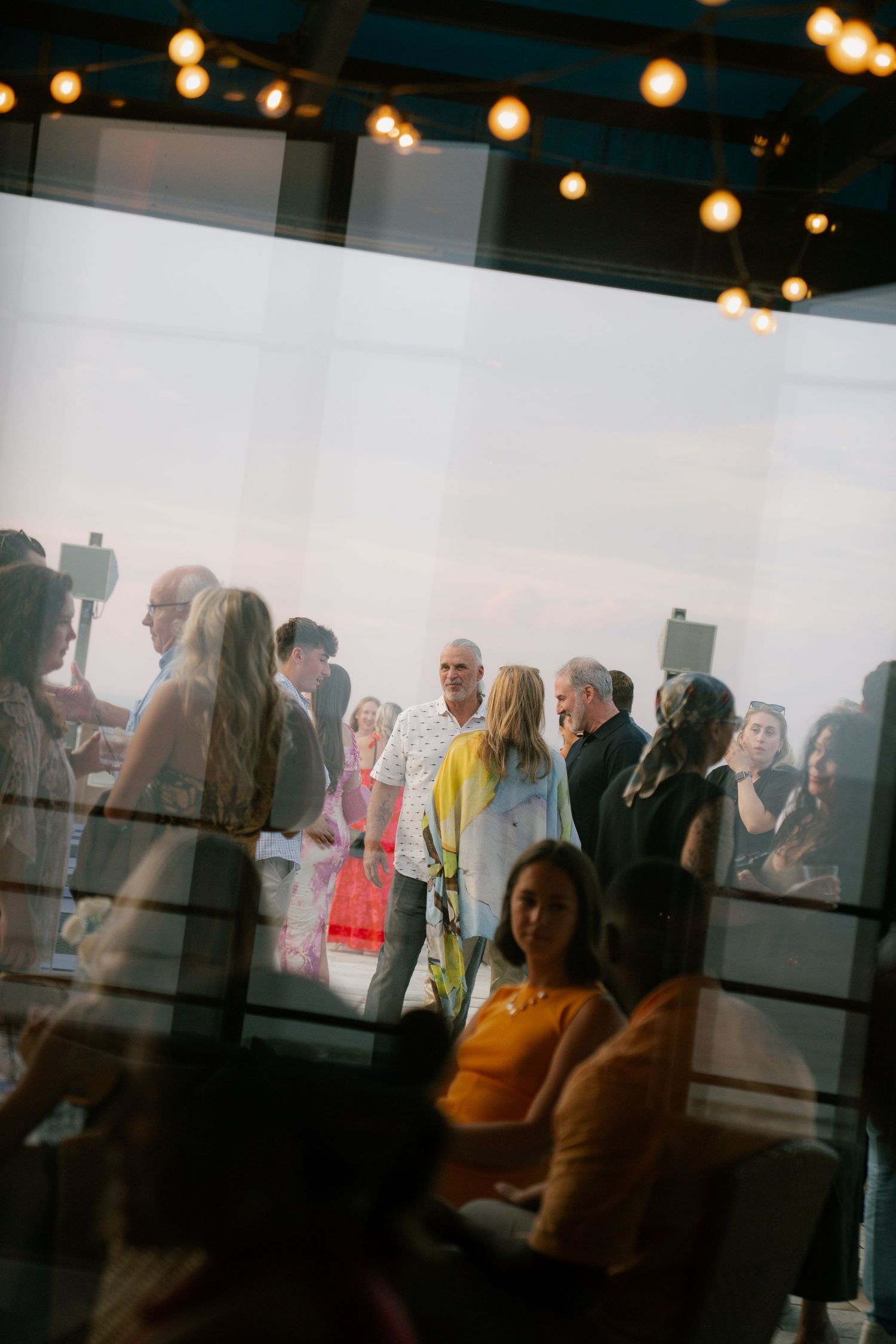Blurred silhouettes of event attendees beneath warm string lights.