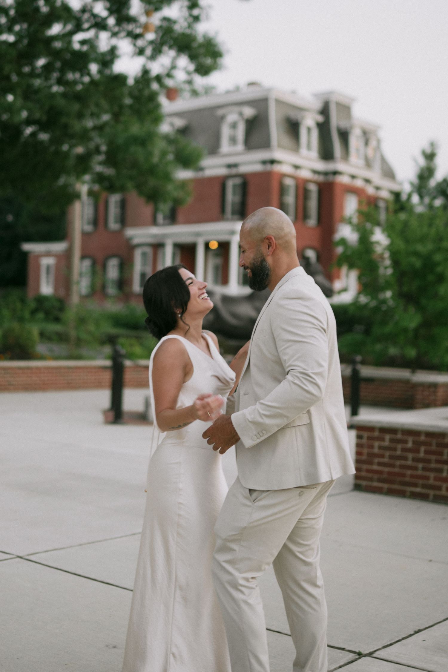 A couple dancing and laughing together on a concrete patio with red brick buildings in the background.