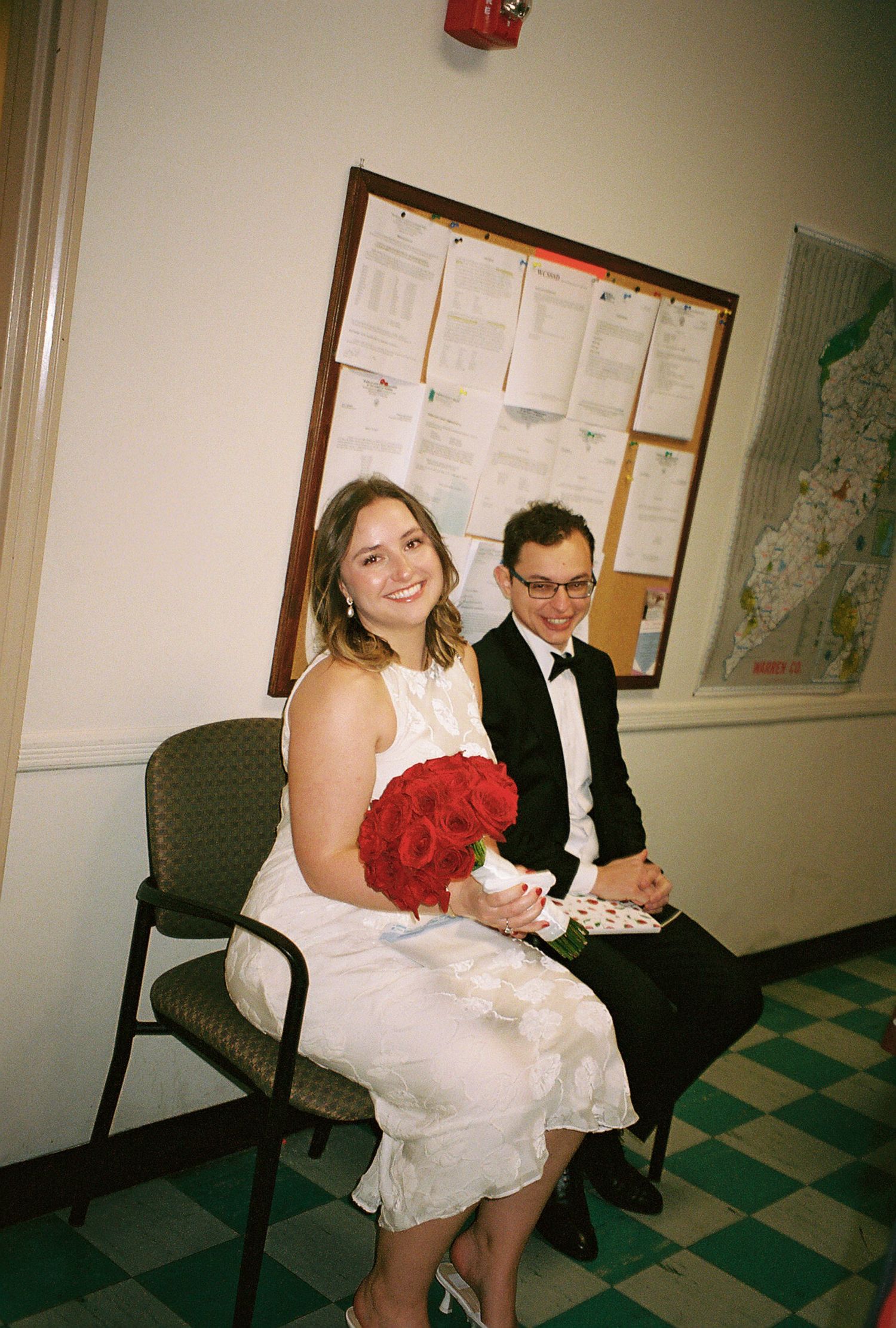 Wedding party waiting in a hallway with checkerboard floor and red bouquet.
