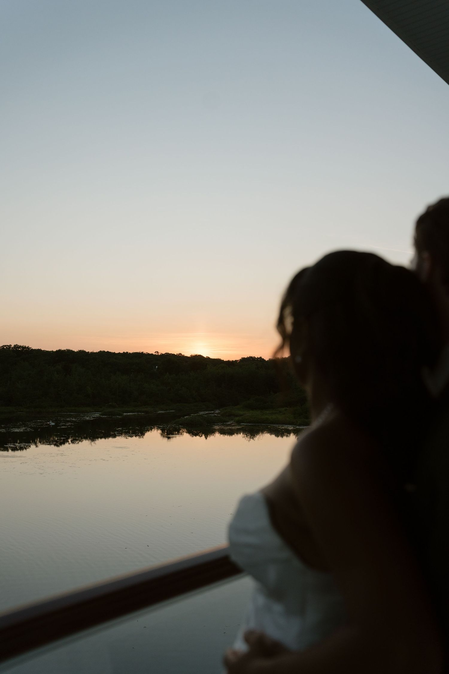 Silhouetted couple watches a golden sunset reflecting over a calm river from a balcony.