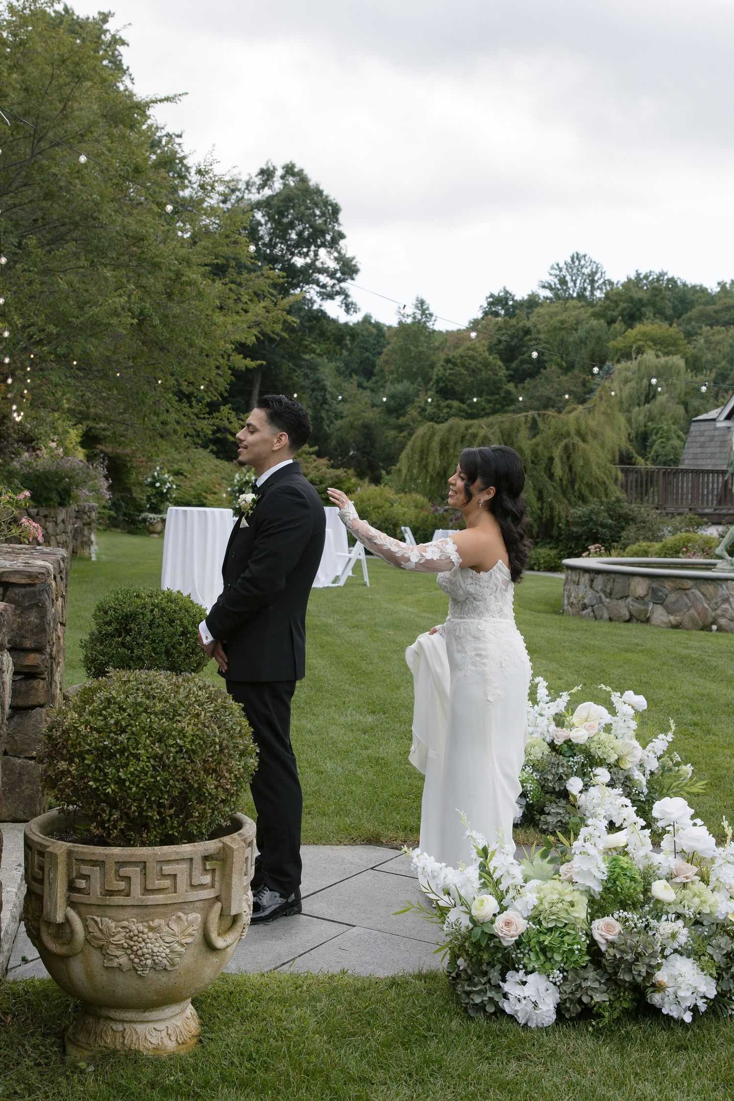 Bride and groom share a first look moment in a lush garden wedding venue with white floral arrangements.