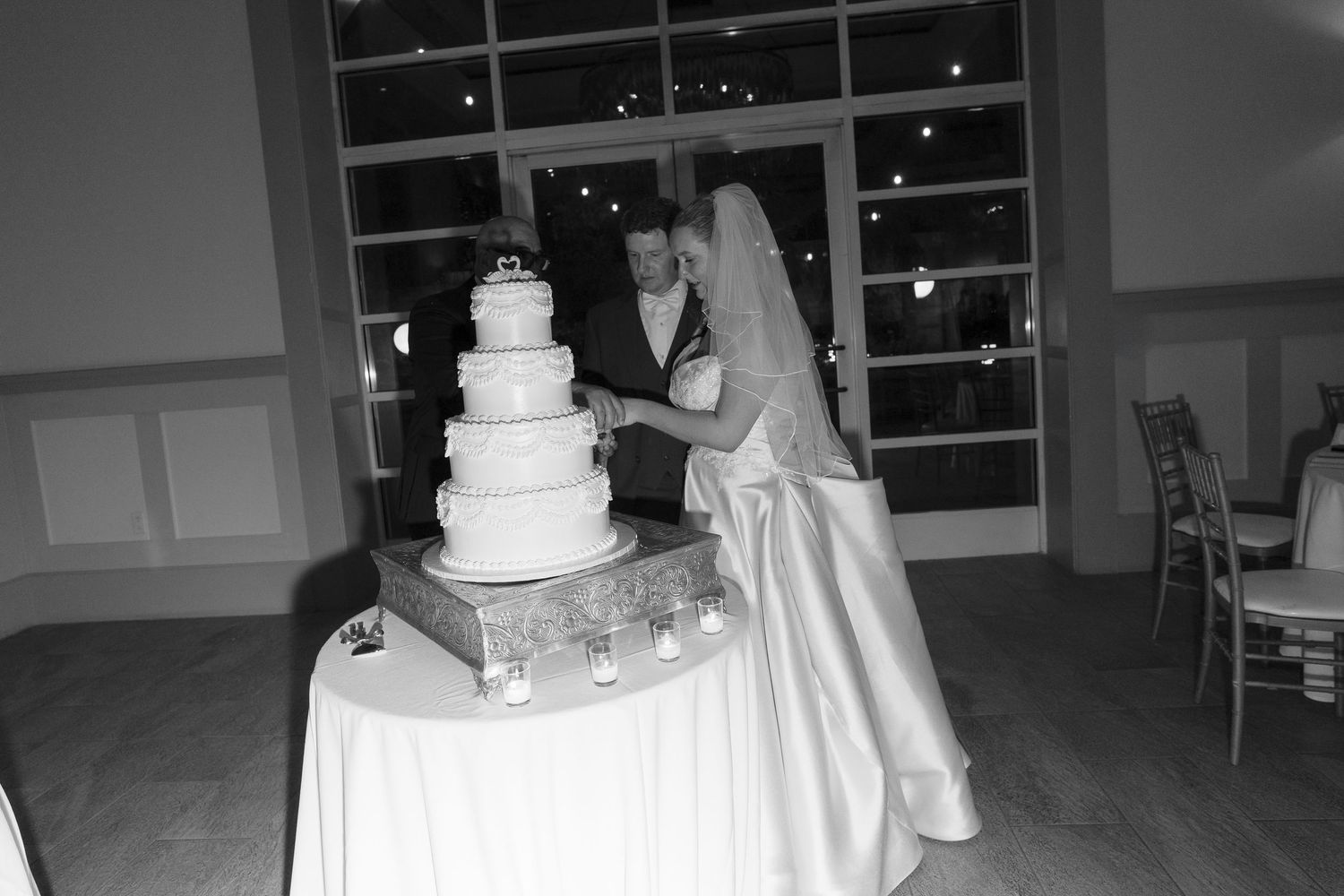Black and white photo of bride and groom cutting their tiered wedding cake at the reception.