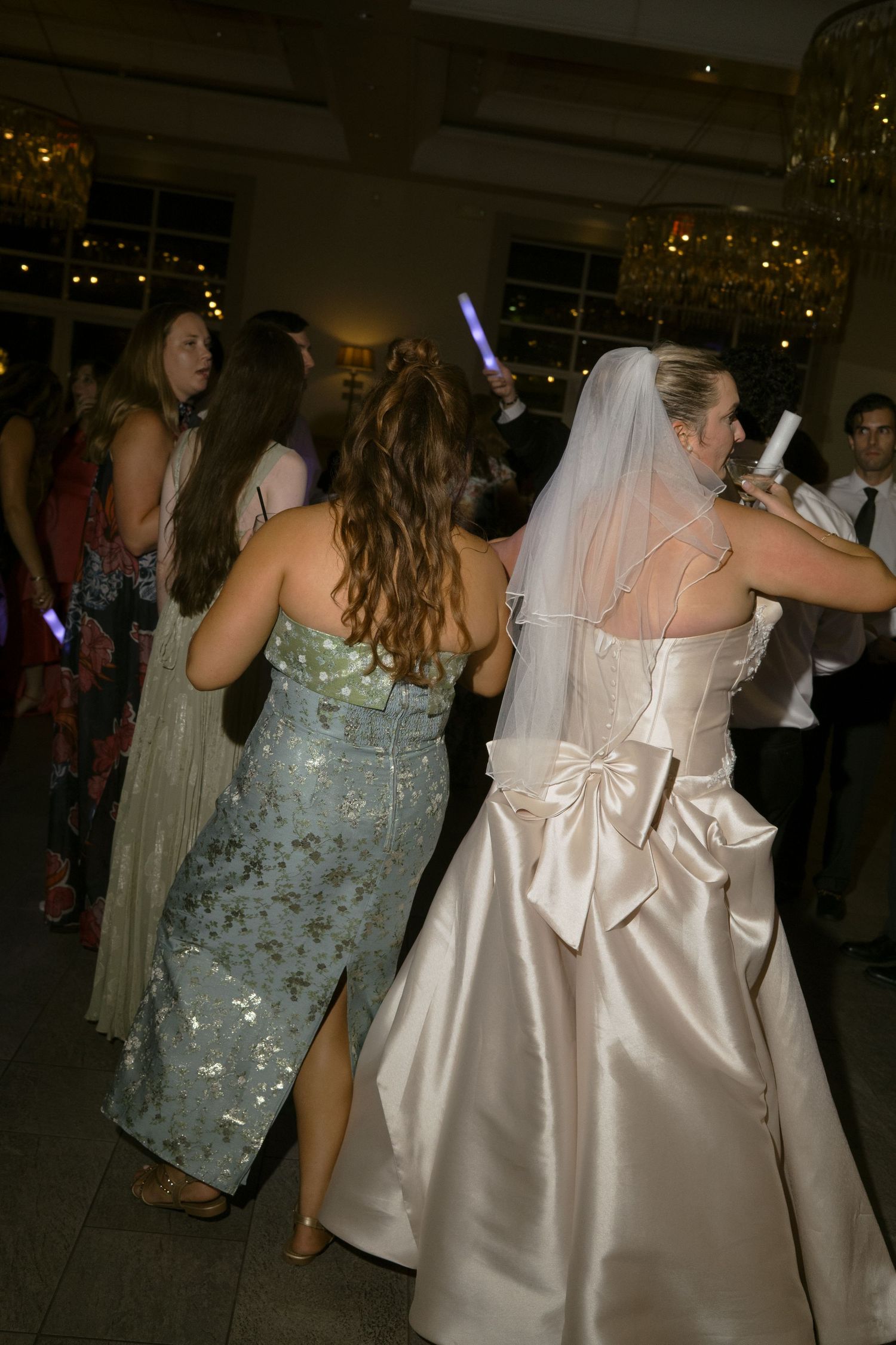 Bride in satin gown with bow back dances with guests at lively wedding reception.