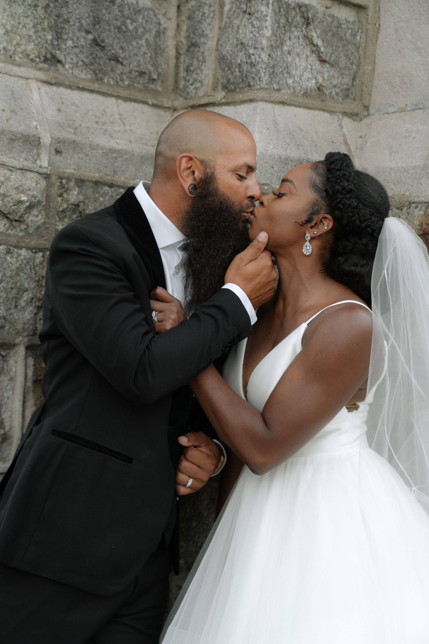 Intimate wedding couple shares romantic kisses against stone wall backdrop.