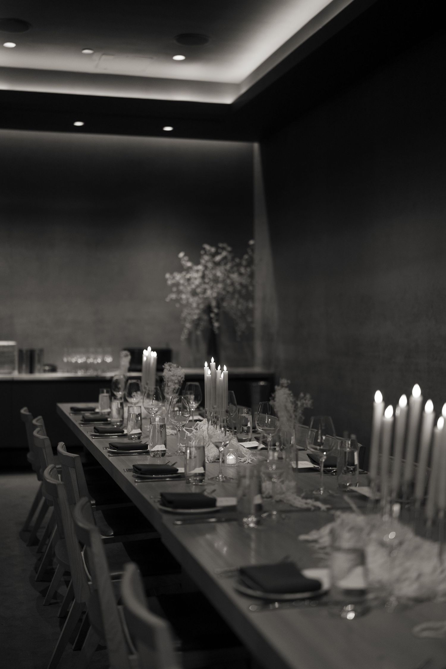 A moody black and white view of an elegant wedding reception table setting with glowing candles.