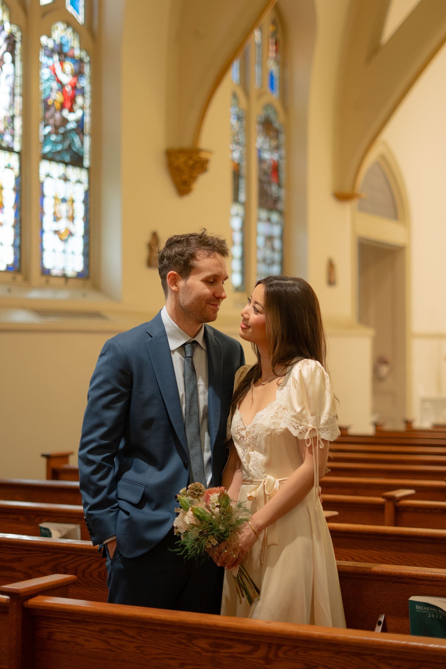 A couple shares a romantic moment in church pews with stained glass windows in the background.