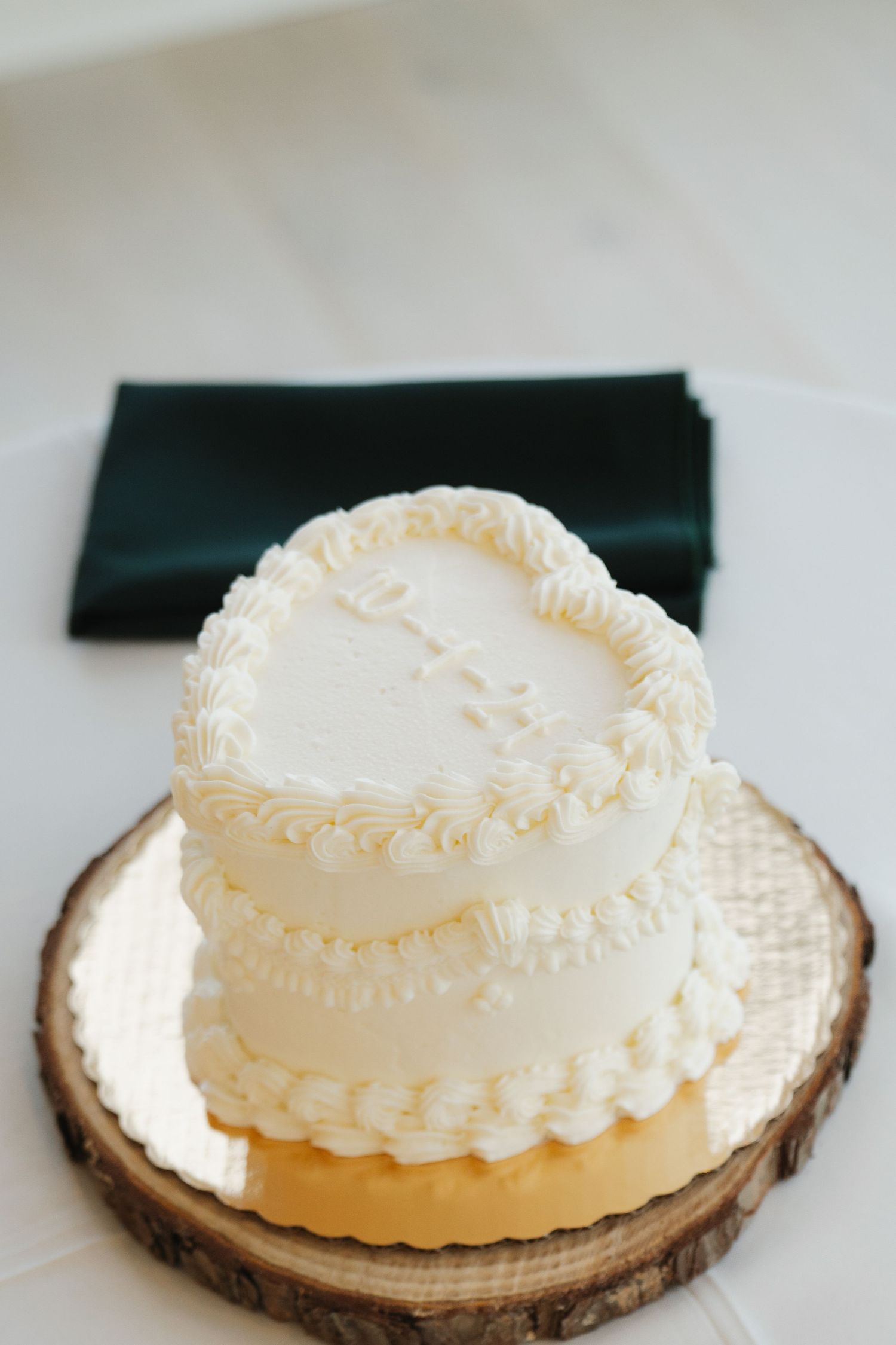 Small two-tier white wedding cake with delicate piped details sits on a rustic wood slice cake stand.