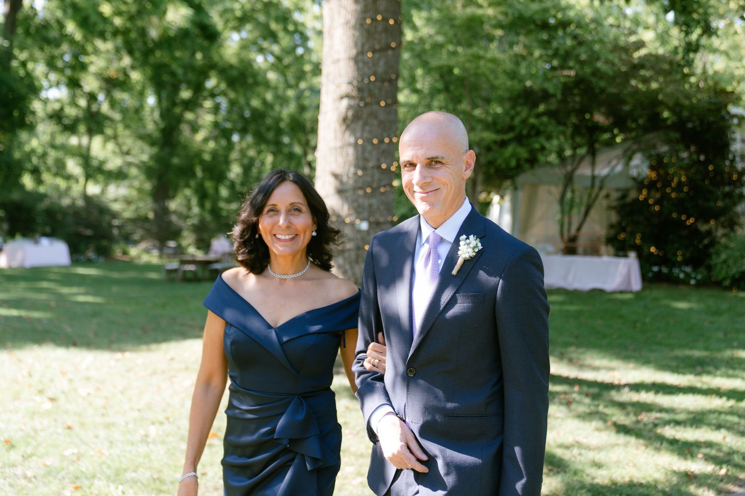 A group of people in formal navy and white attire pose together outdoors in a garden setting.
