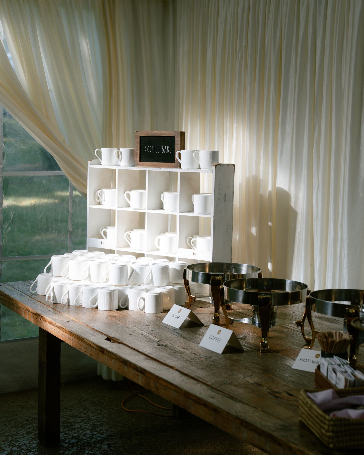 Long wooden table with place settings and white name cards under elegant draped fabric.