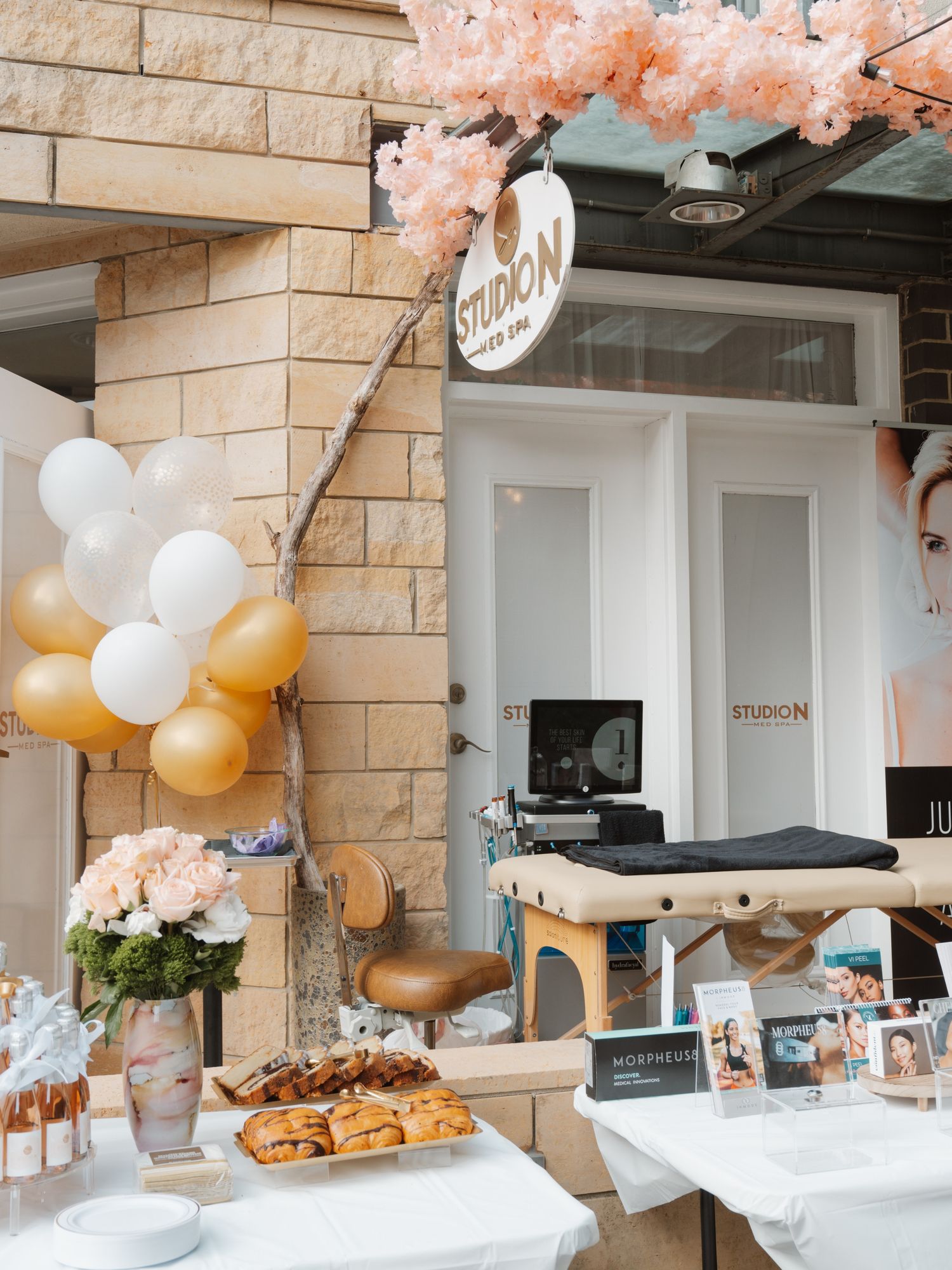 Modern event space decorated with pink cherry blossoms, gold balloons, and white table settings.