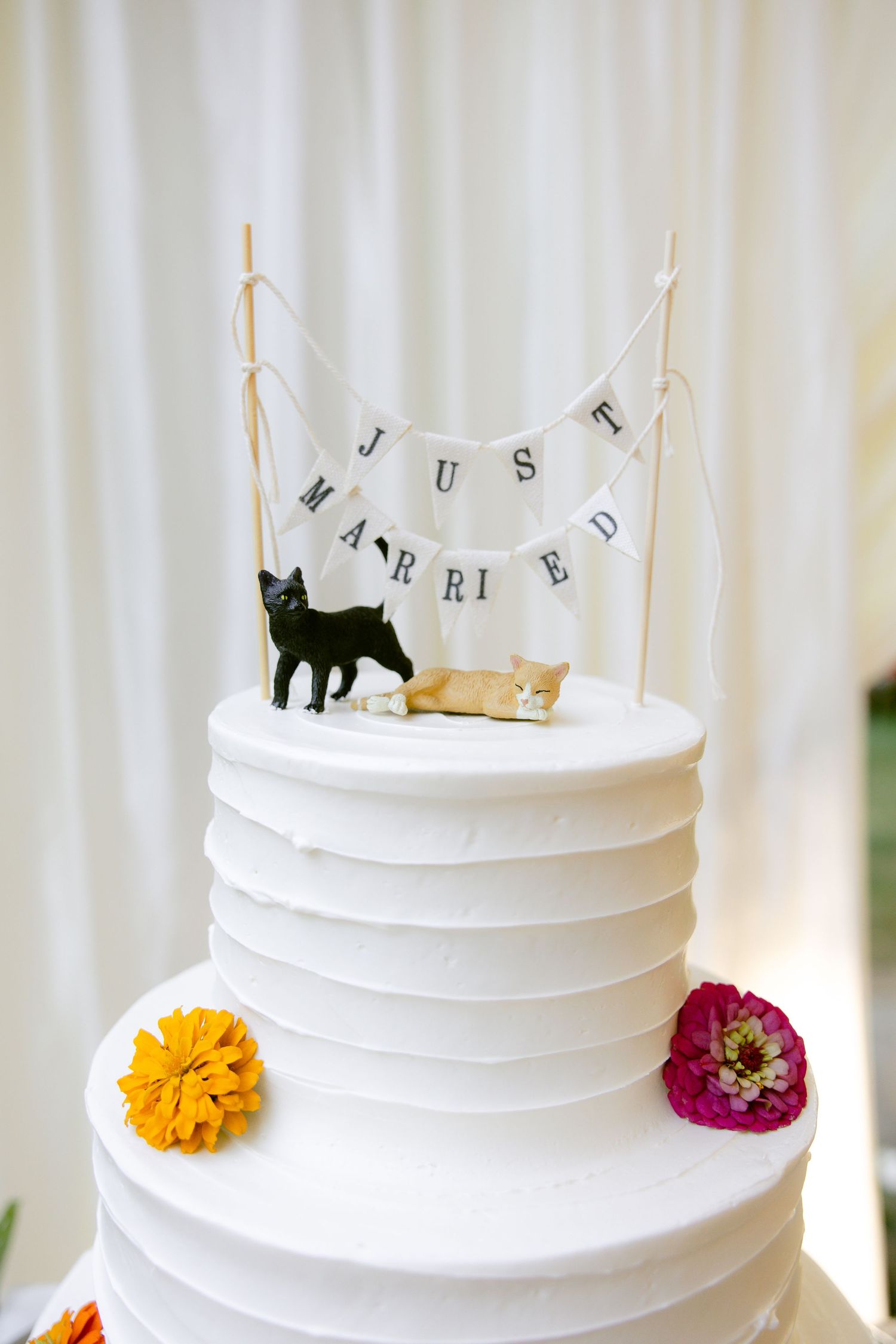 White tiered wedding cake with cat cake toppers and 'Just Married' banner.