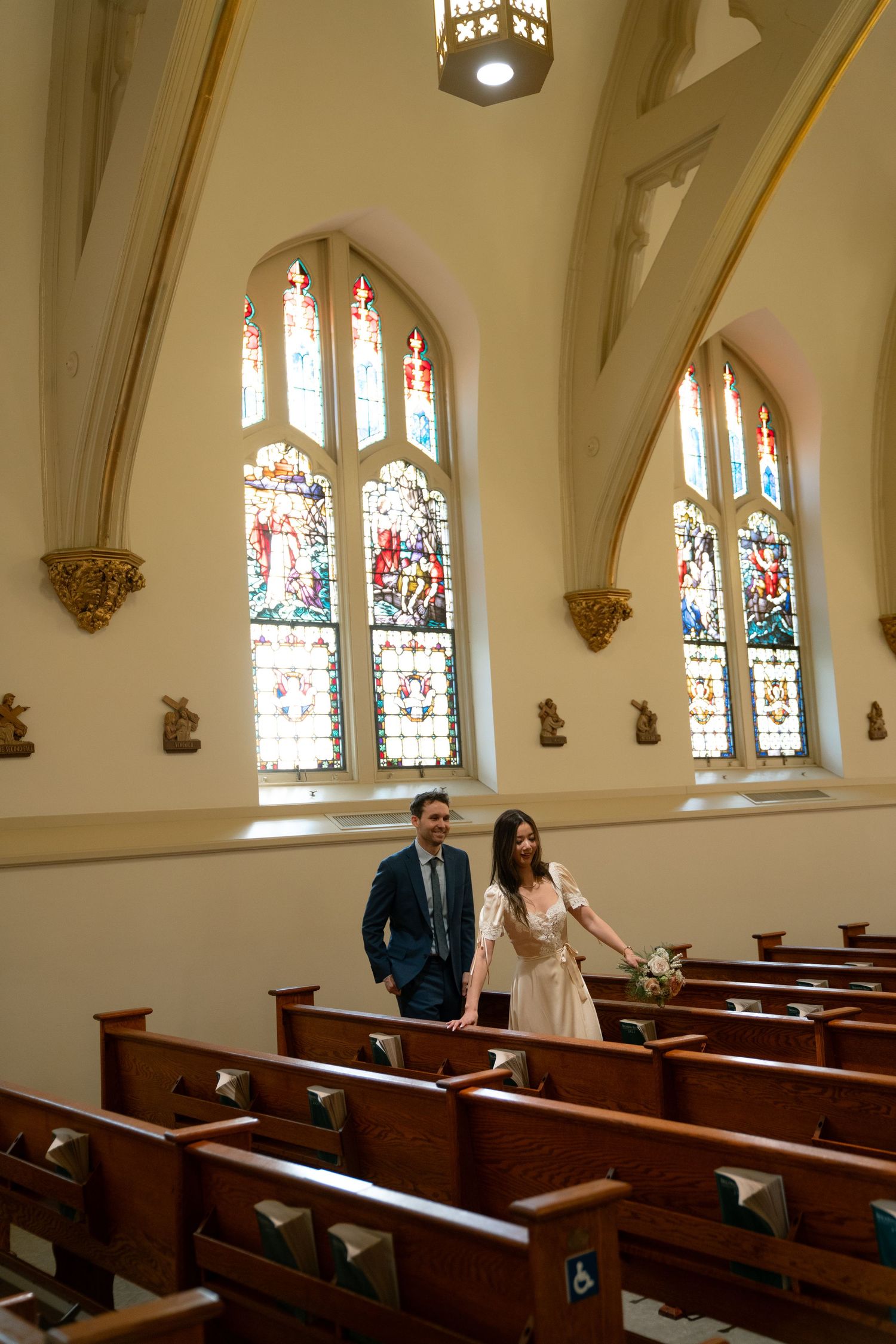 Sunlit church interior with wooden pews and stained glass windows during an intimate wedding ceremony.