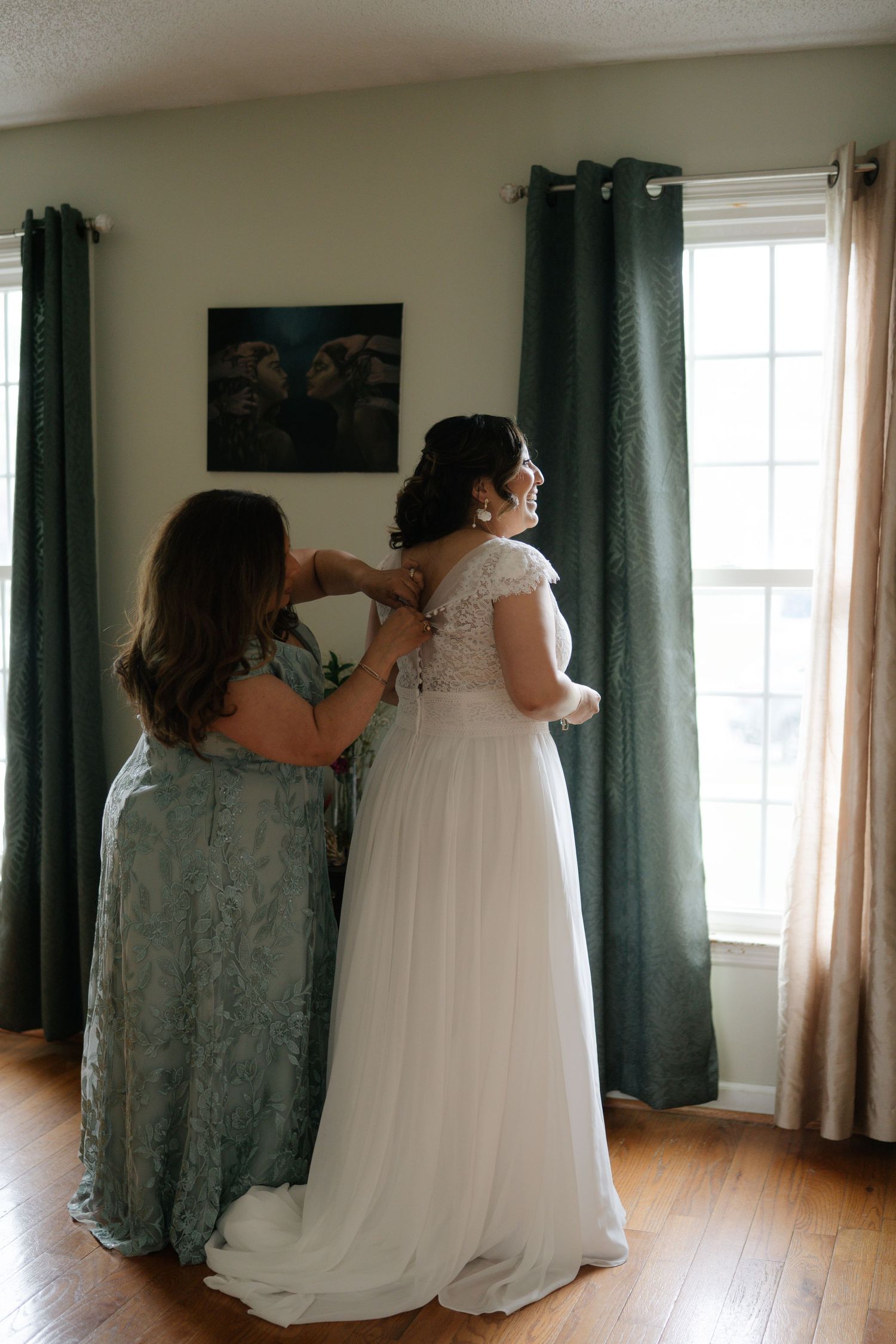 A wedding dress fitting moment as someone helps adjust the back of an elegant white gown.