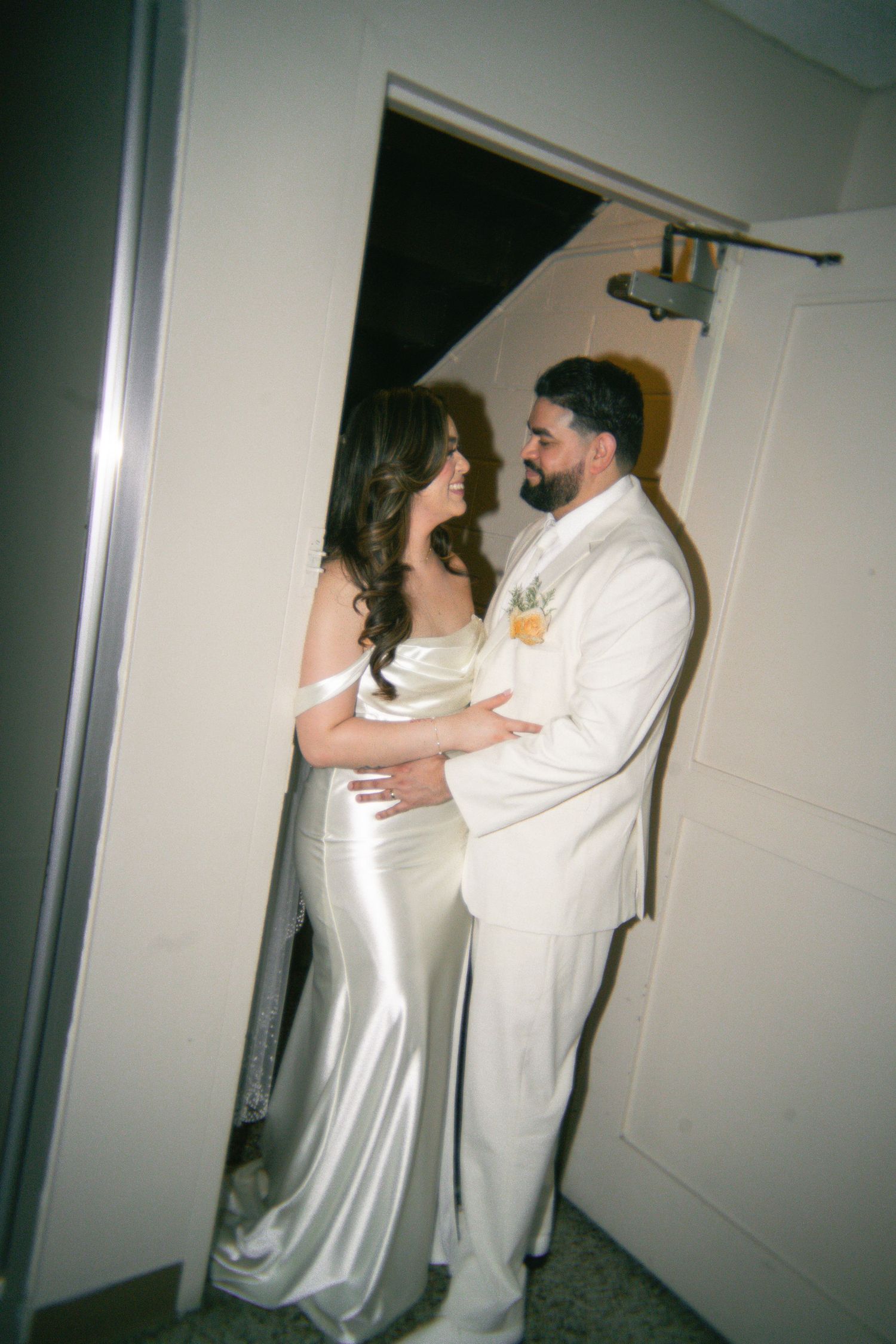 A couple in white outfits playfully dance and pose in a hallway.