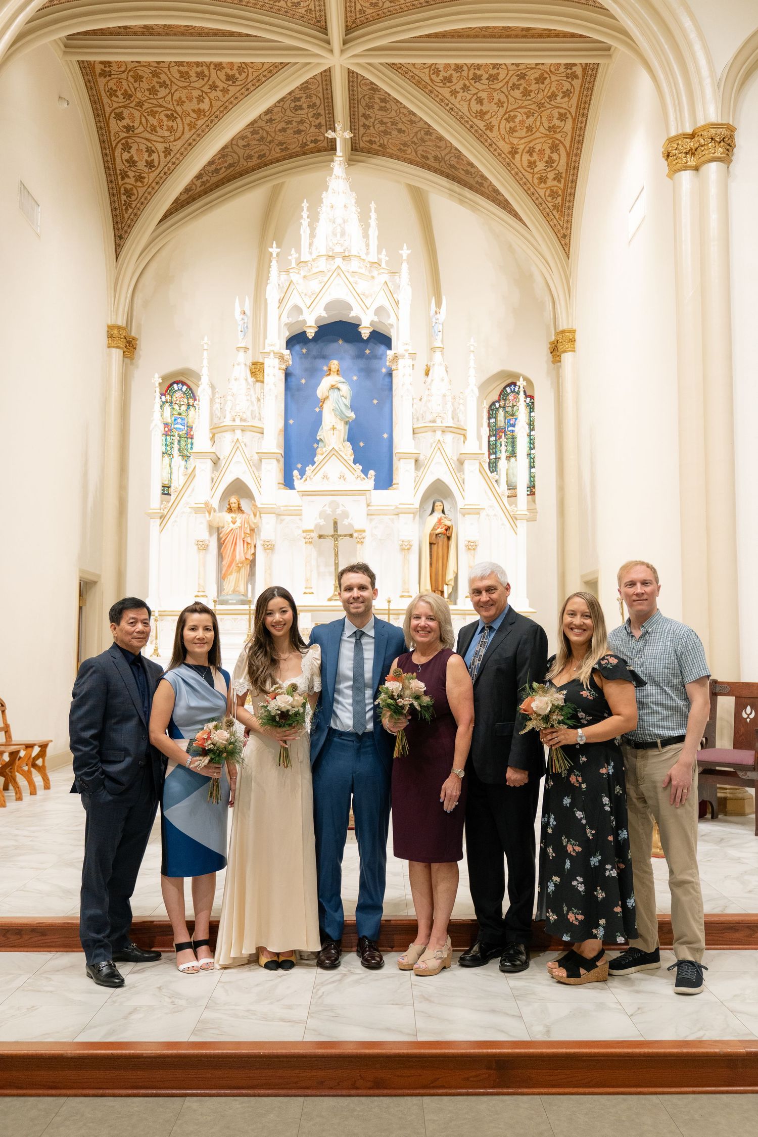 Wedding party members gather for formal group photos inside an ornate church with white and gold decor.