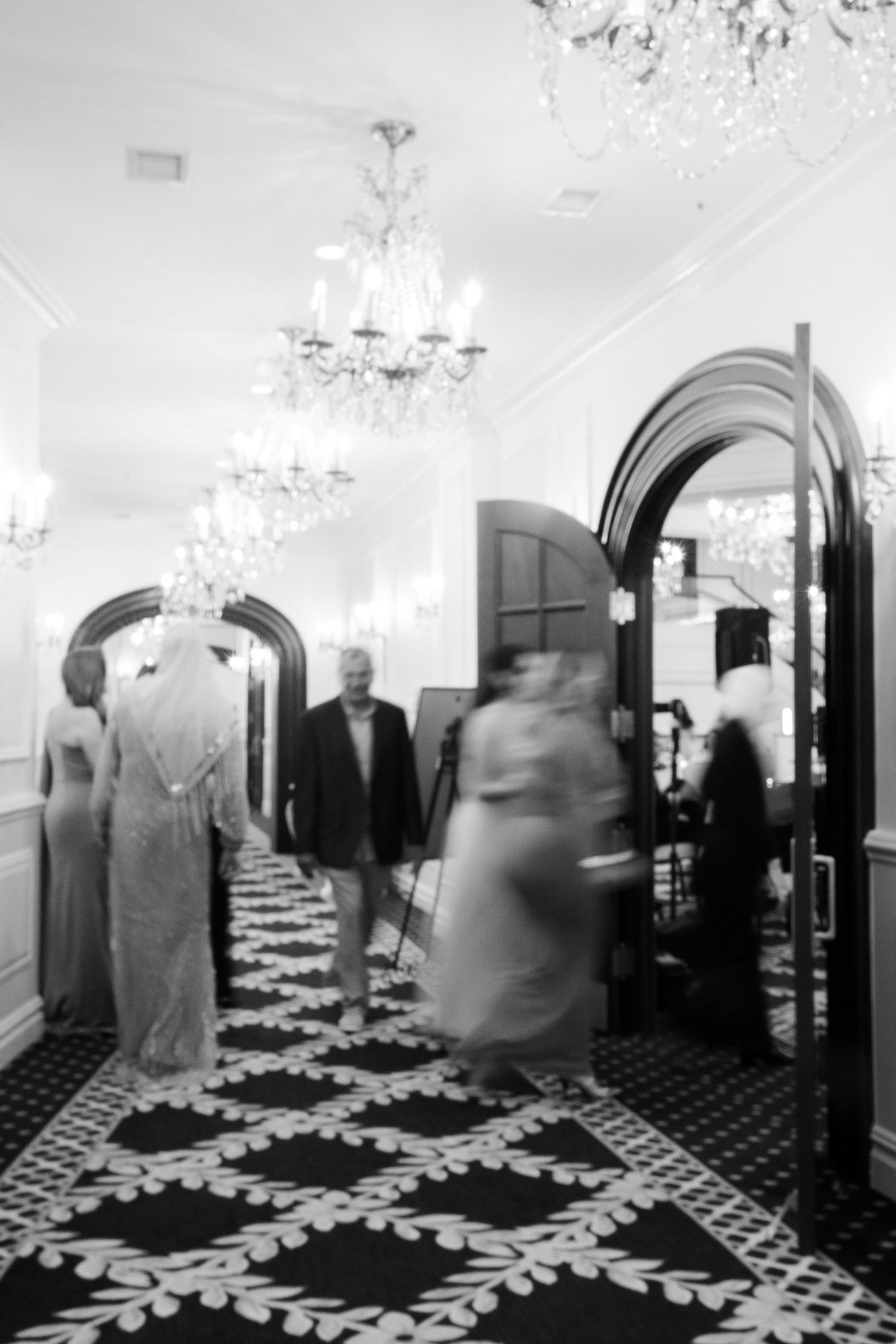Black and white sequence of people moving through an elegant hallway with patterned flooring.