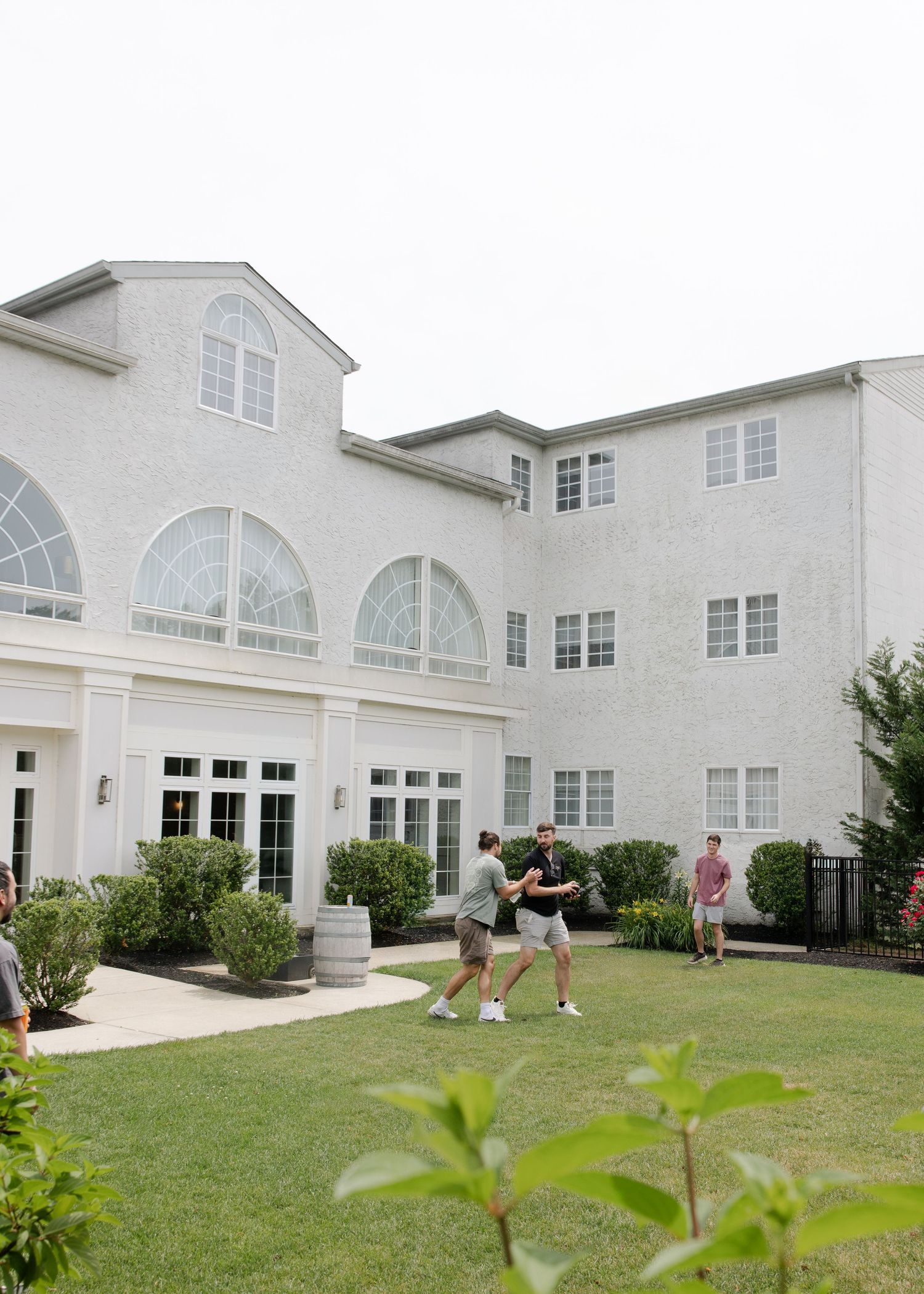 Guests play lawn games on green grass outside a elegant white multi-story wedding venue.