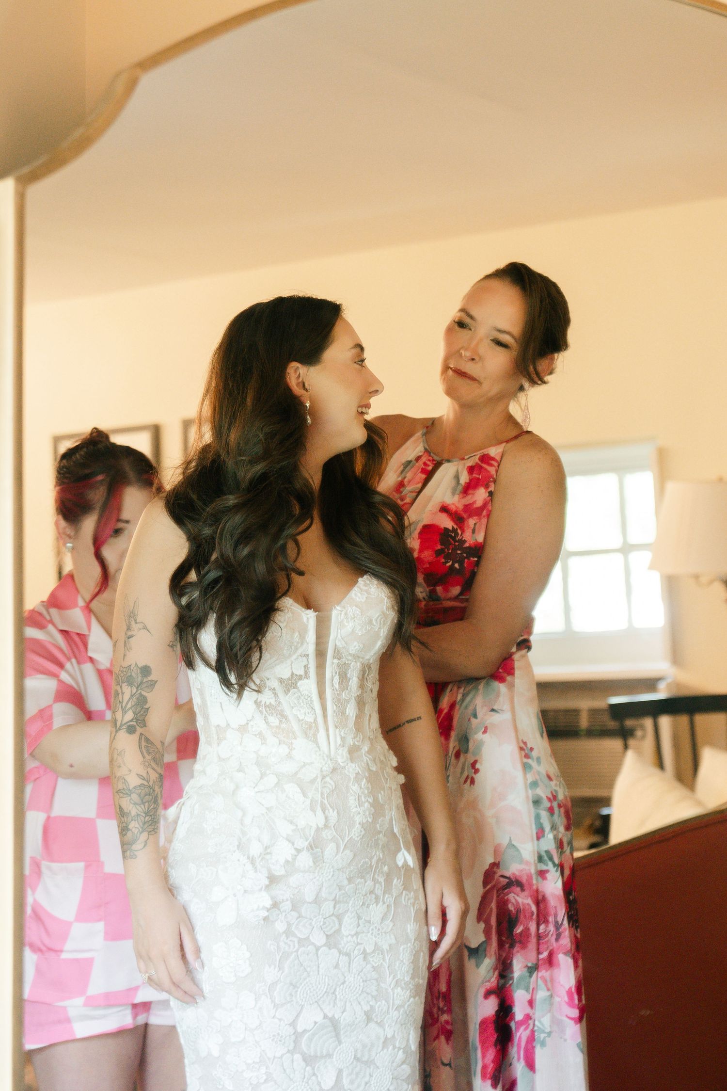 Wedding party getting ready in a sunlit room with white and pink floral dresses.