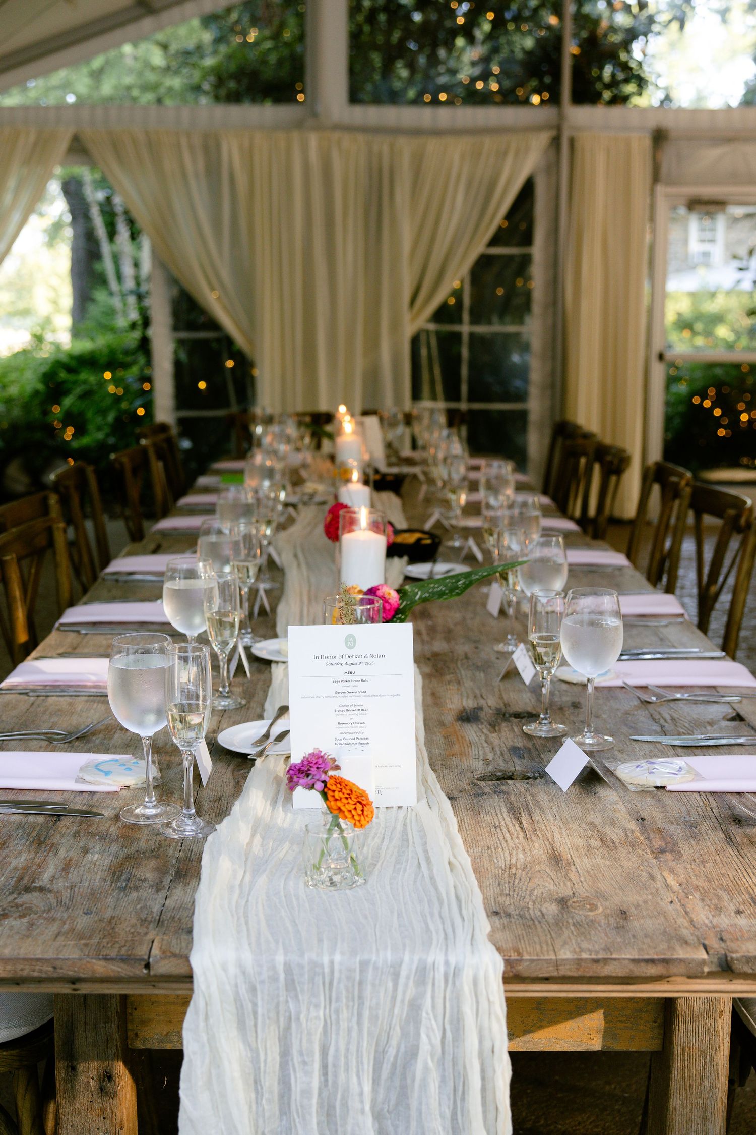 Rustic farmhouse tables with white runners and place settings under an outdoor tent for a wedding reception.