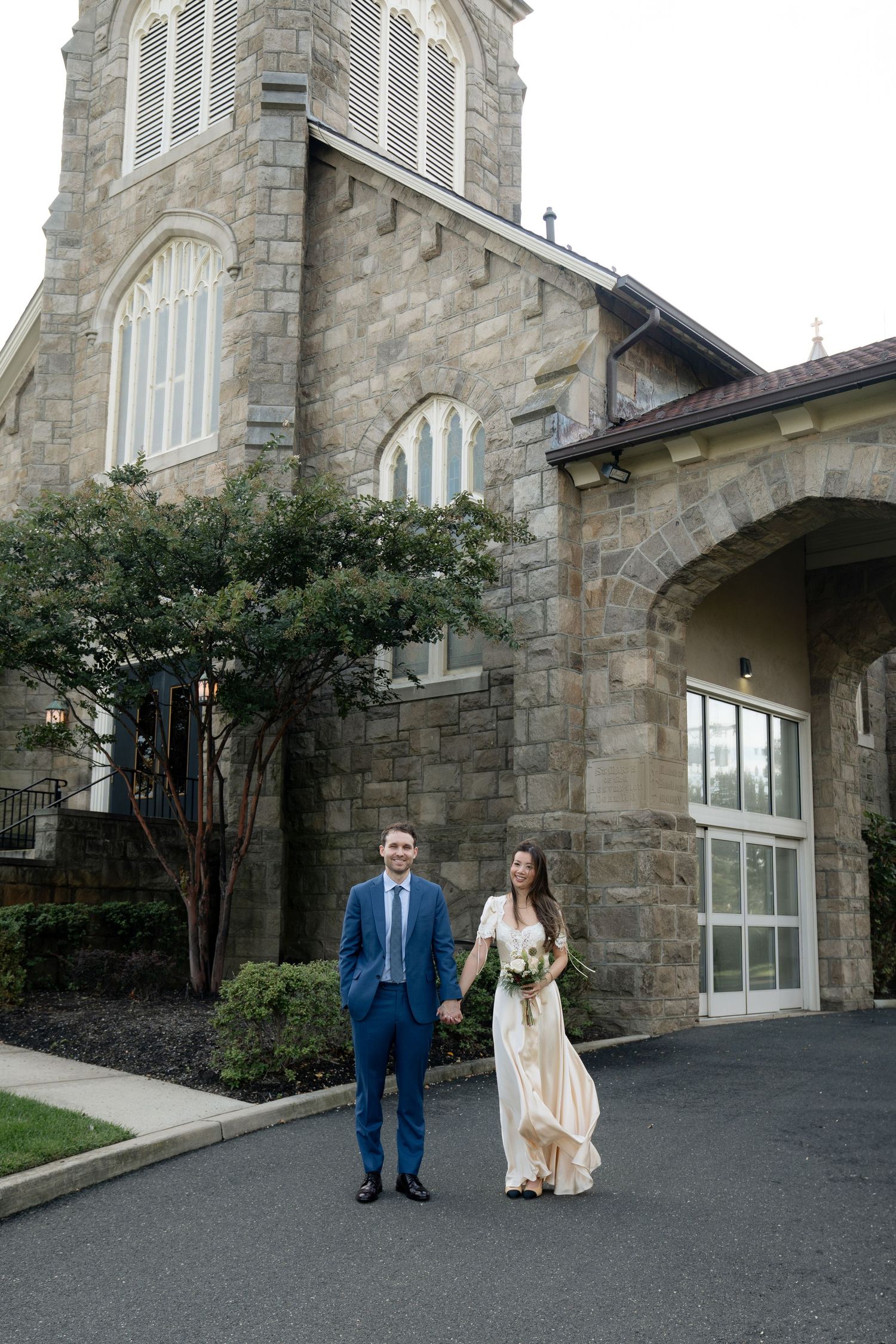 A couple poses outside a grand stone church building with gothic architecture.