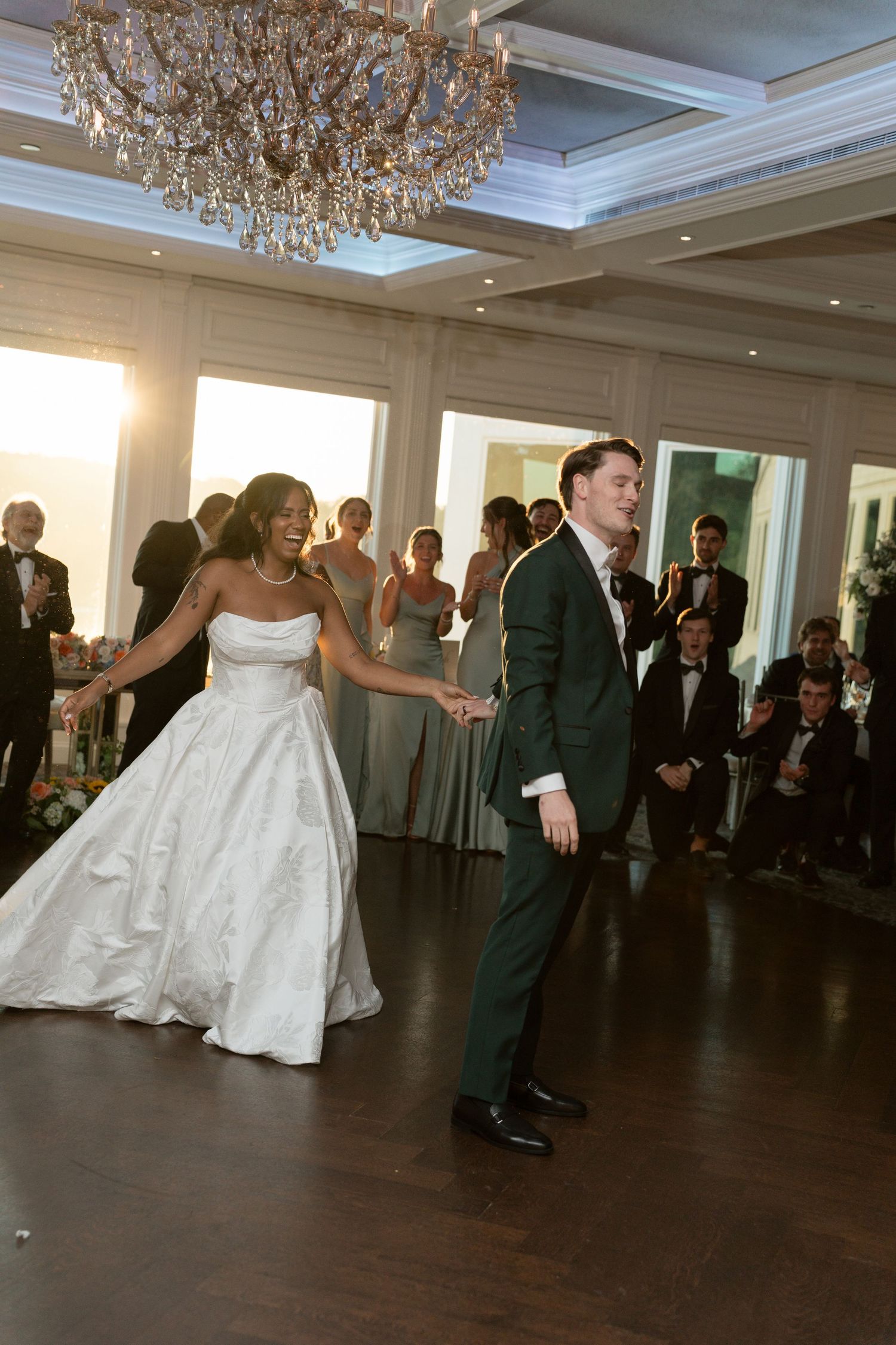Bride and groom share their first dance under a crystal chandelier at elegant wedding reception.