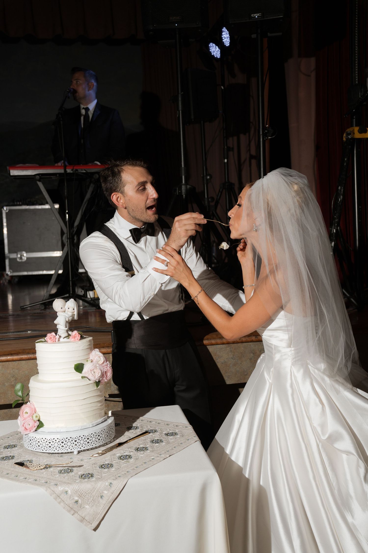 Bride and groom cutting and sharing their elegant three-tier white wedding cake during their reception.