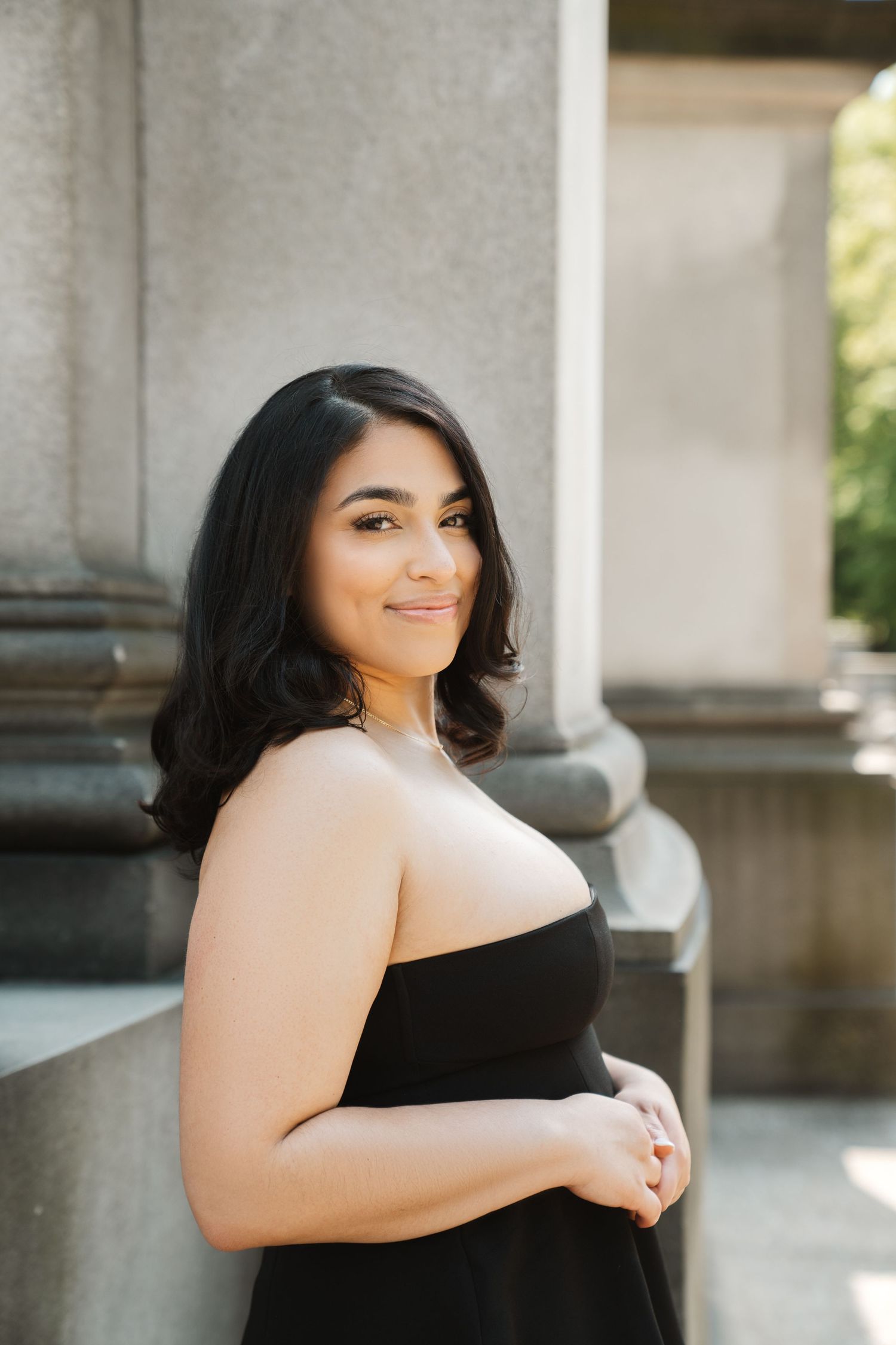 Professional portrait series in black dress against architectural columns with natural lighting.