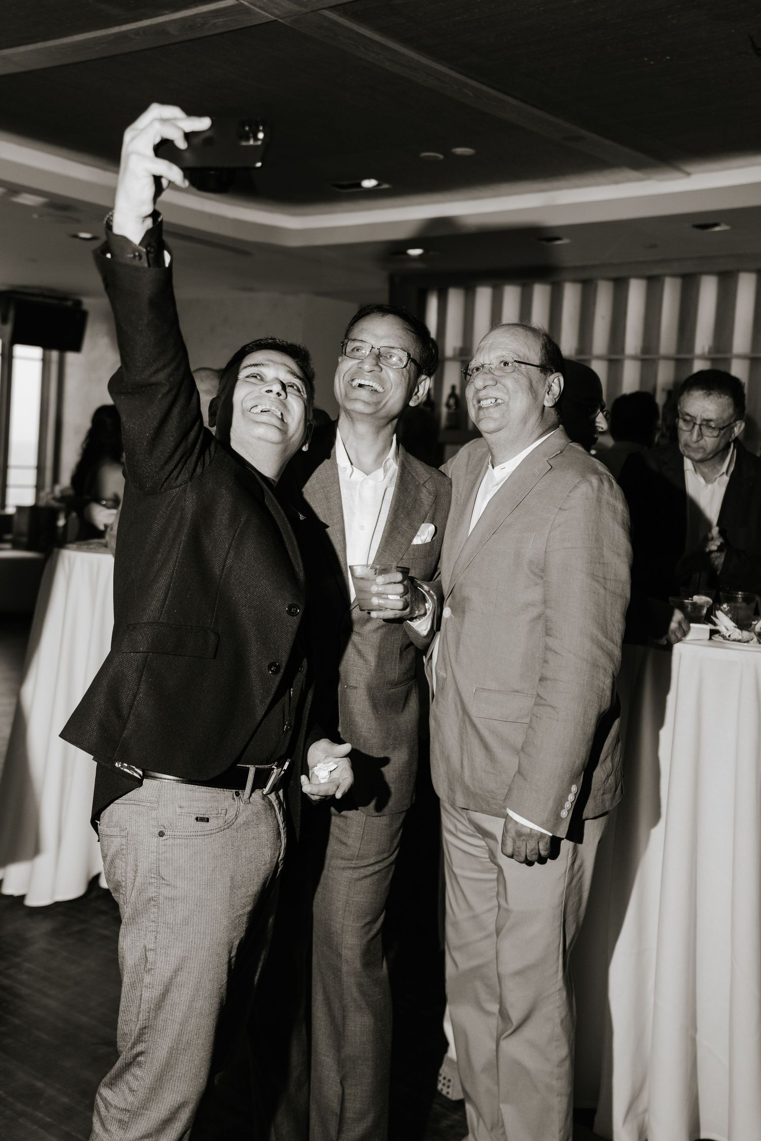 Black and white photo of groomsmen celebrating with raised arms at indoor reception.