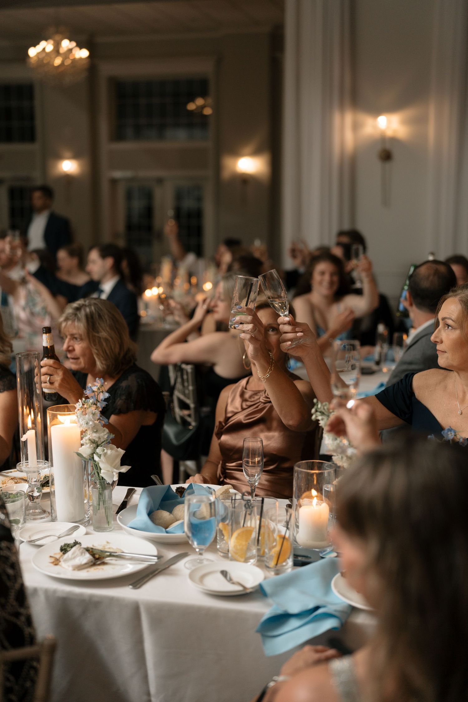 Wedding guests raise champagne glasses in a toast during elegant candlelit reception dinner.