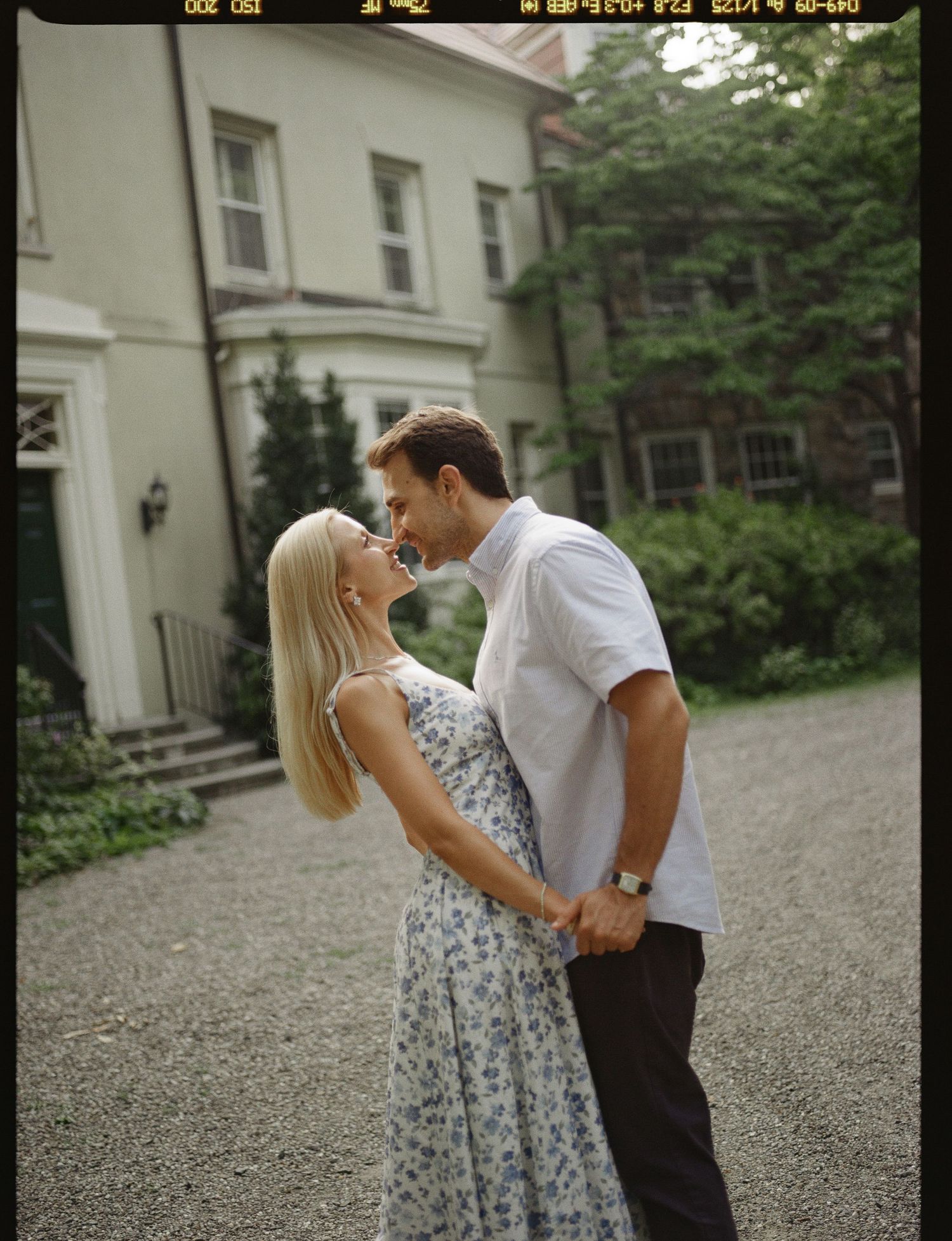 Couple sharing a romantic moment outdoors, holding hands near a charming green house surrounded by lush trees.