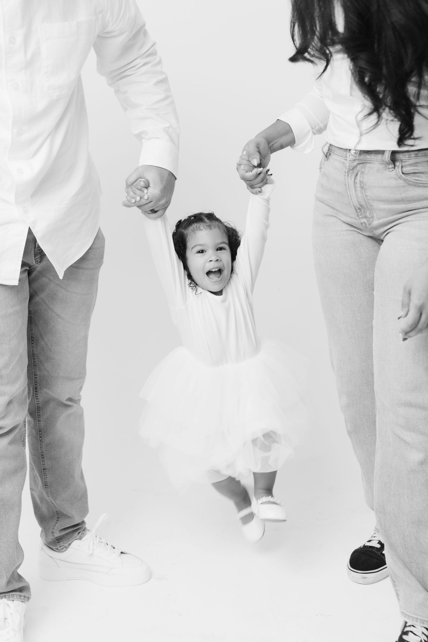 A joyful family moment captured in black and white as a small child jumps while holding hands with adults.