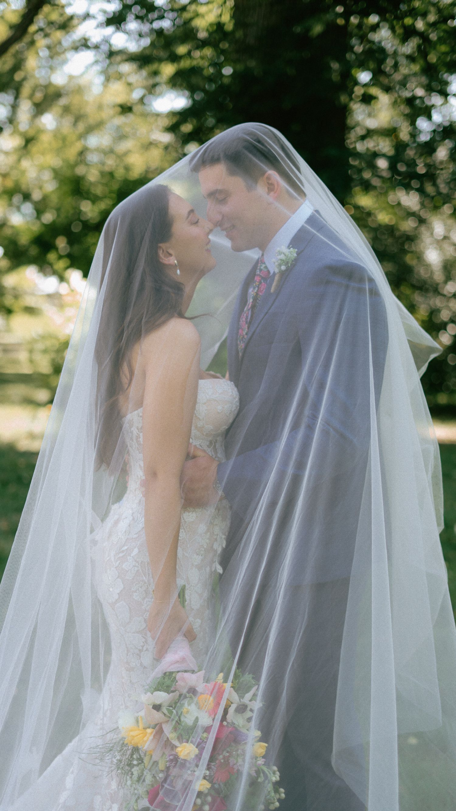 Romantic wedding couple sharing tender moments under a flowing white veil in a garden setting.