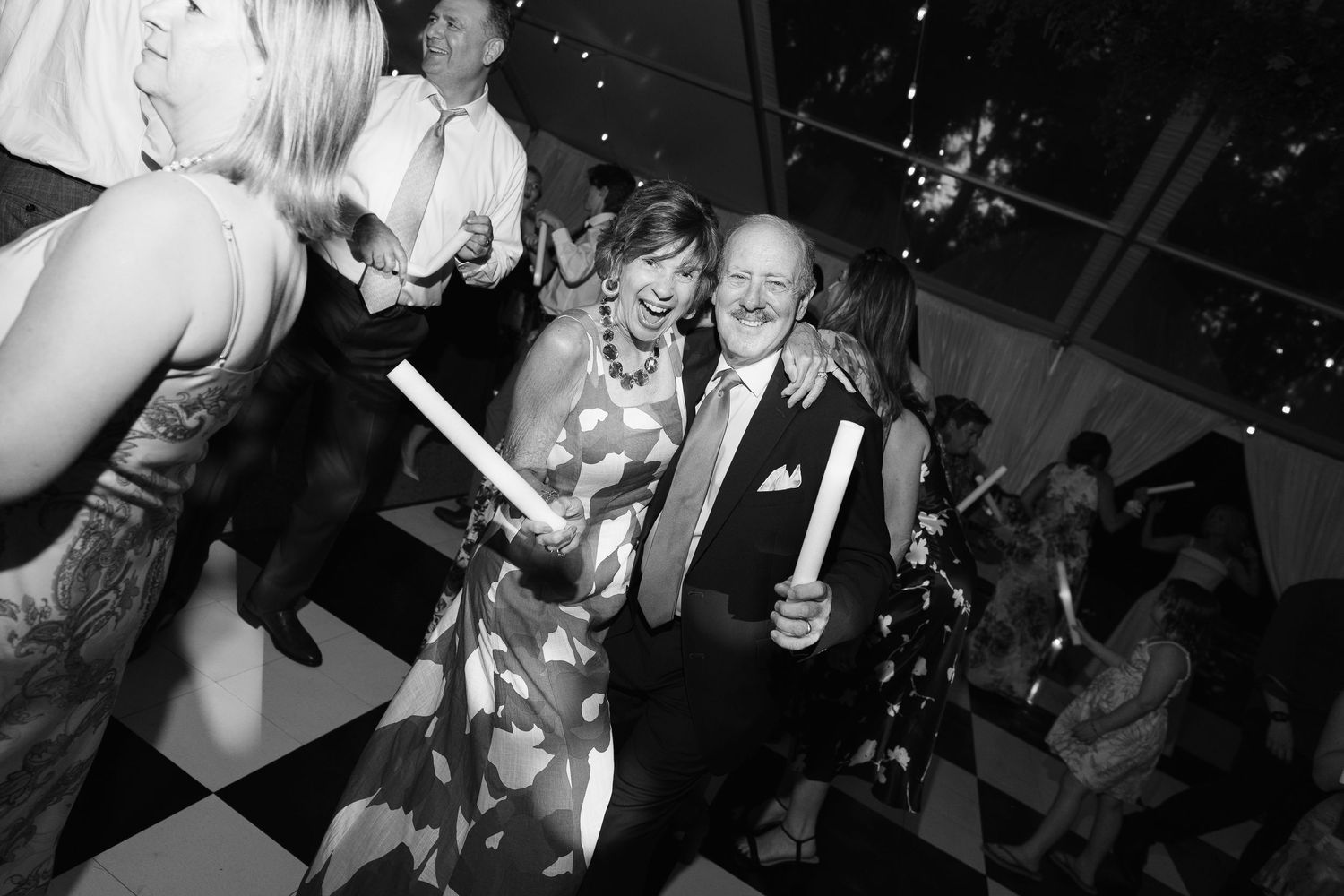 Wedding guests dance and celebrate on a dark dance floor with confetti falling from above during a reception party.