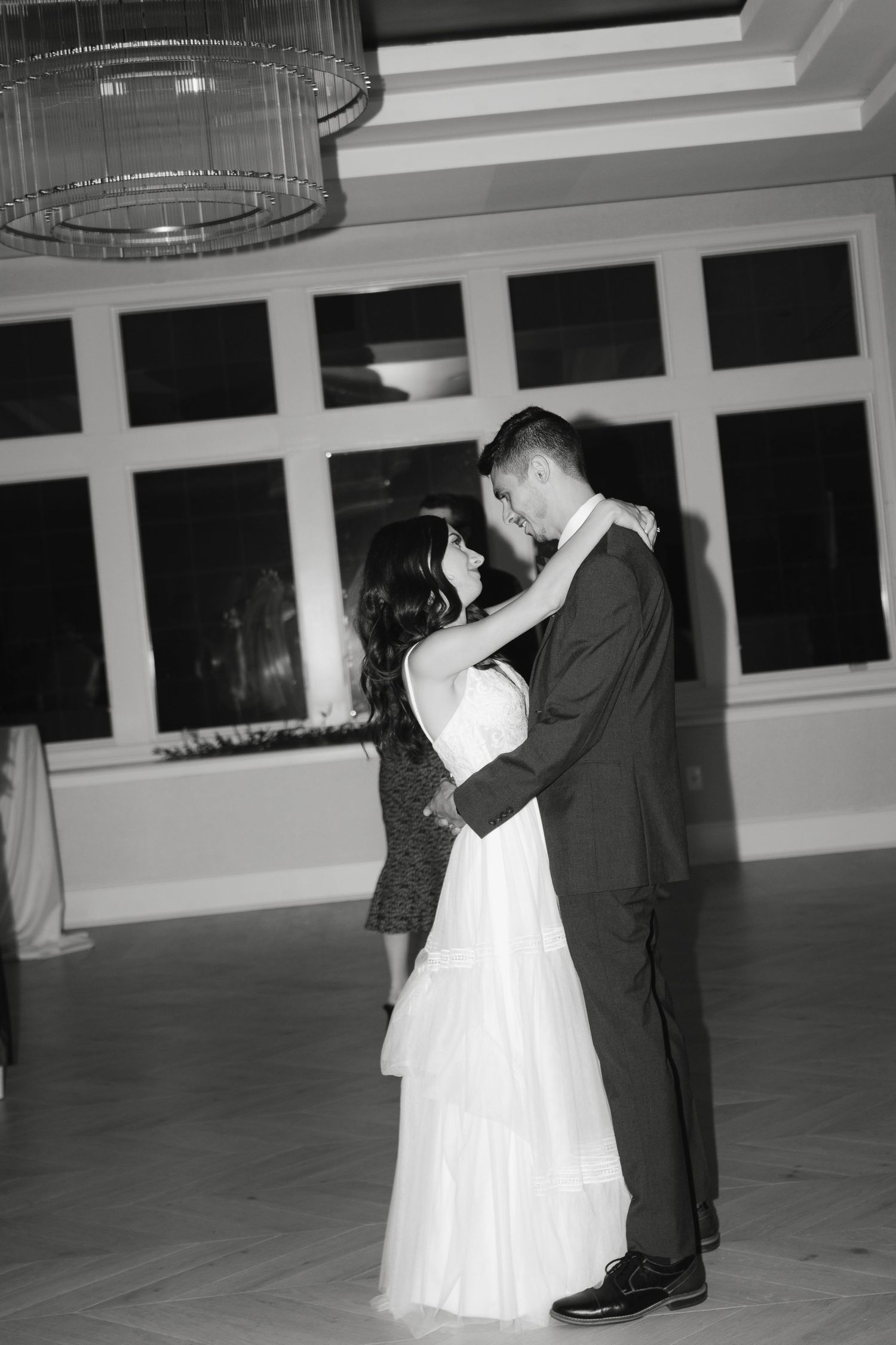 A couple shares their first dance as newlyweds on an elegant ballroom floor under circular chandeliers.