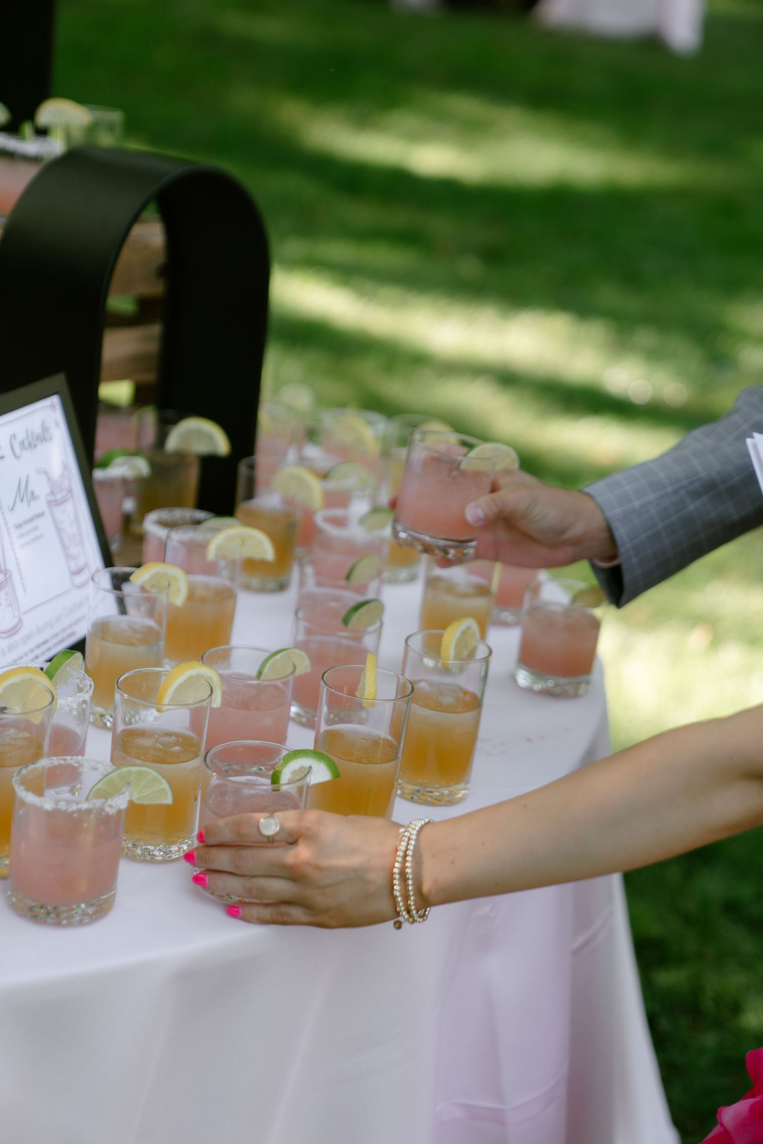 Array of pink and orange cocktails garnished with citrus on an outdoor reception table.