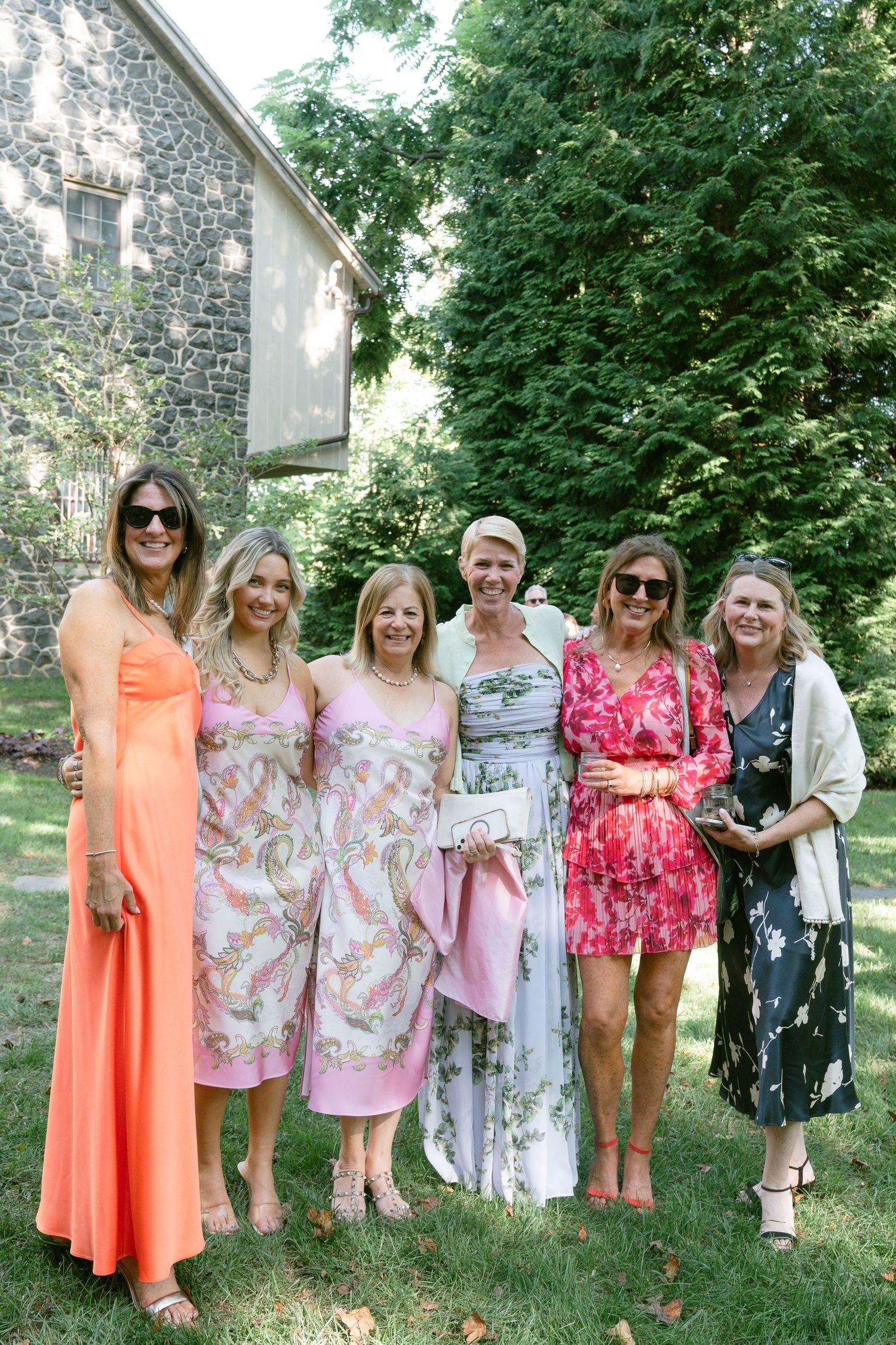 A group of wedding guests in colorful summer dresses posing together on a lawn.