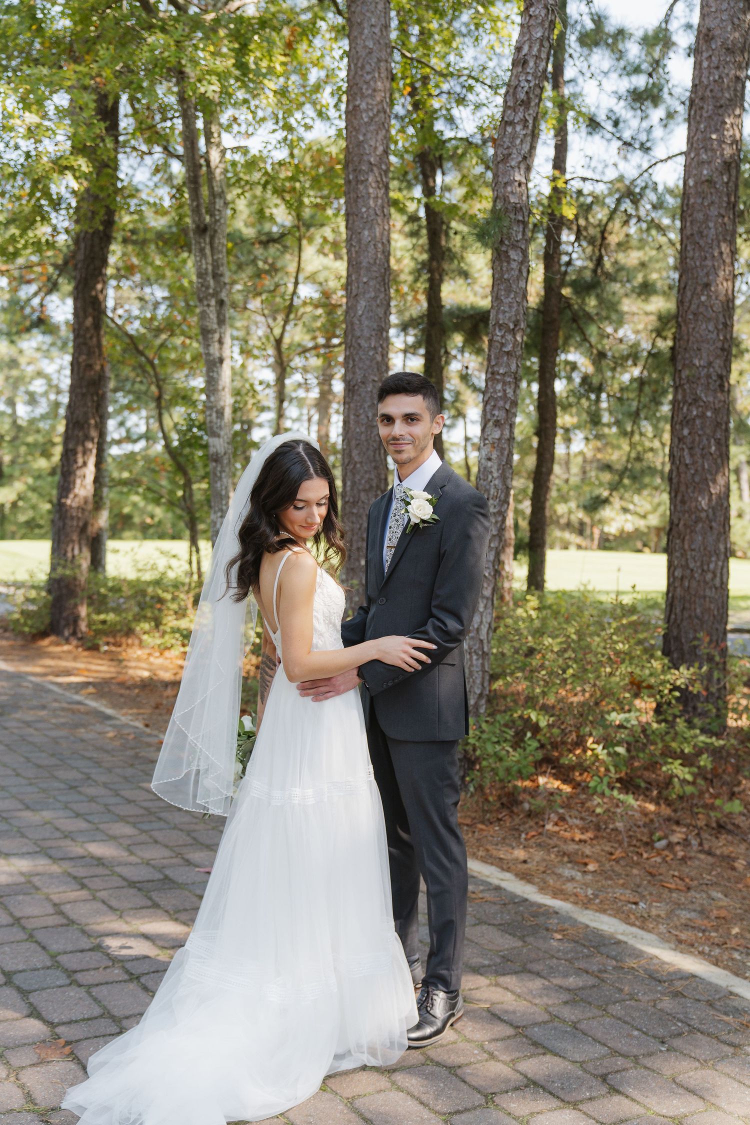 A couple shares romantic moments on a stone path surrounded by tall pine trees during their outdoor wedding celebration.