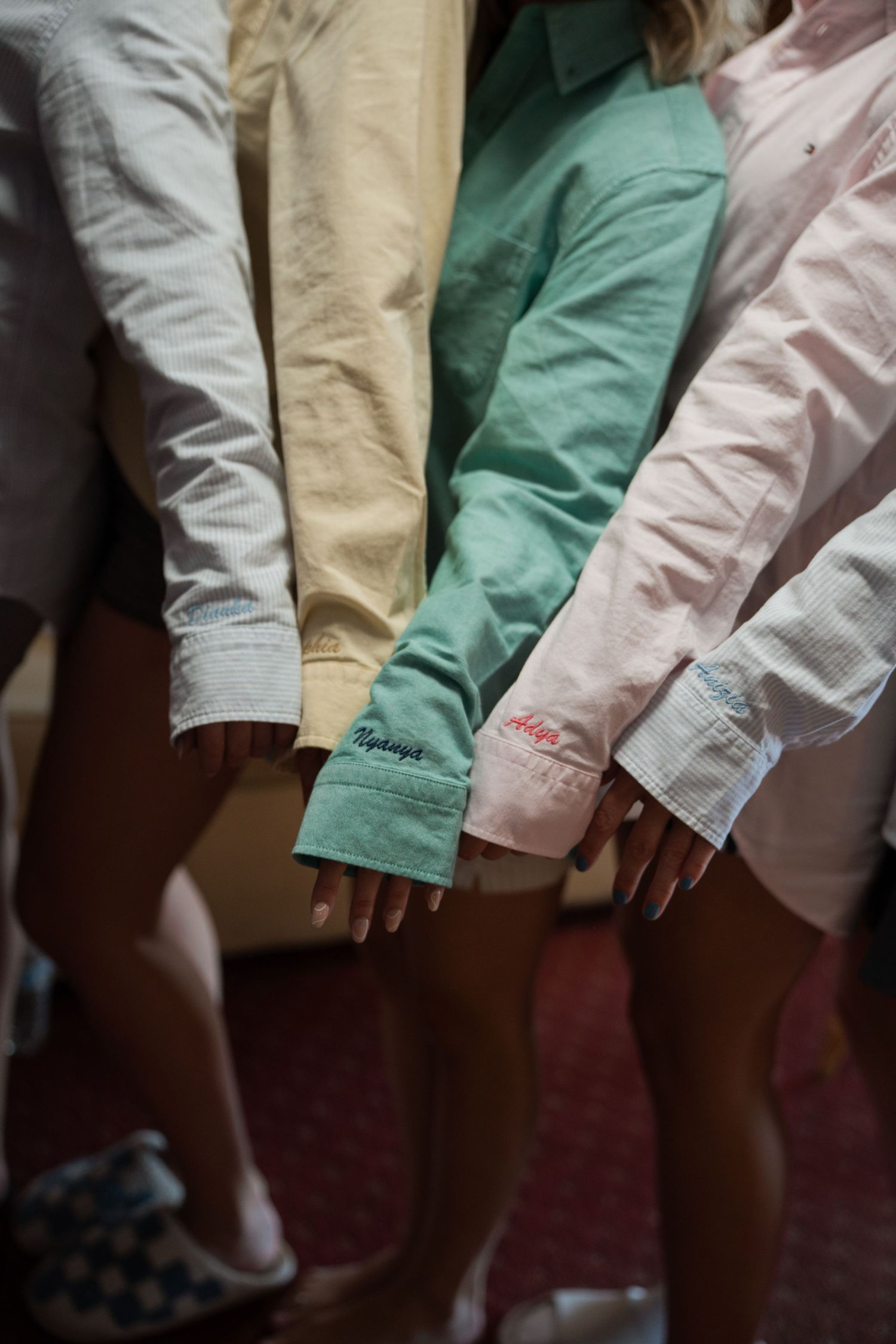 Group of people wearing pastel button-down shirts with embroidered cuffs in white, yellow, green, and pink colors.