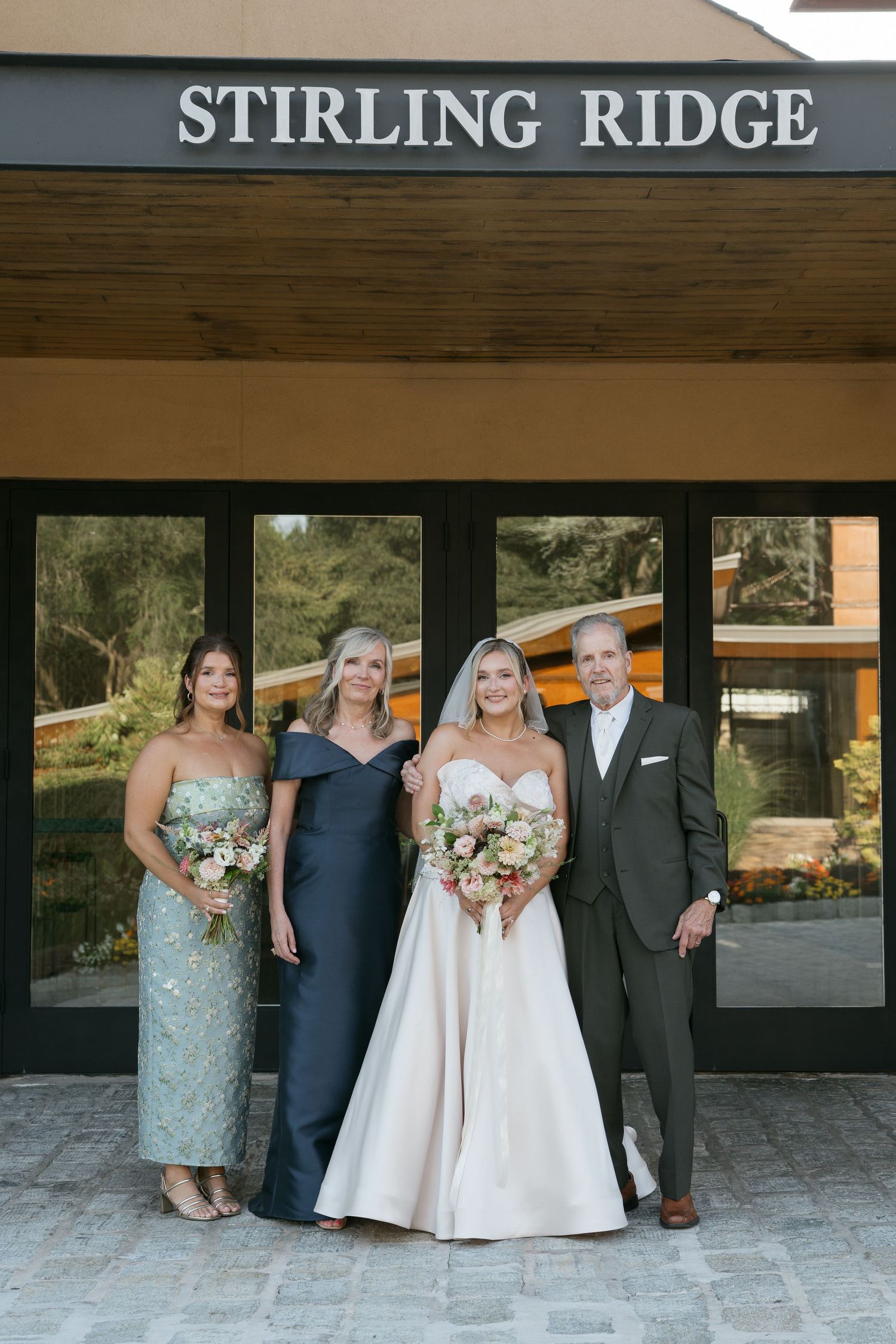 Bride in white gown poses with family outside Stirling Ridge venue, holding pastel bouquets.