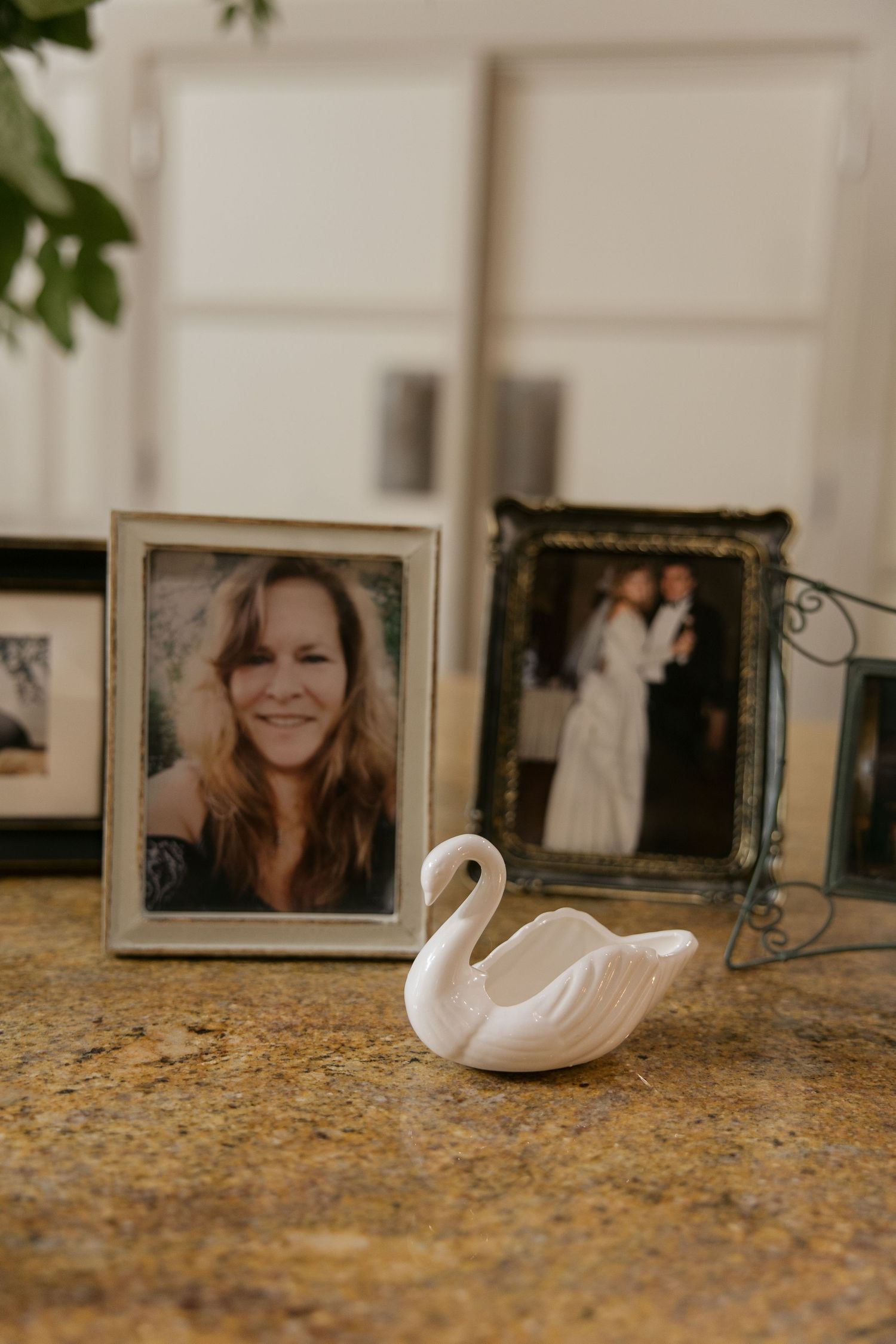 Framed portrait photo of smiling woman displayed on granite countertop with ceramic swan figurine and wedding photo in background.