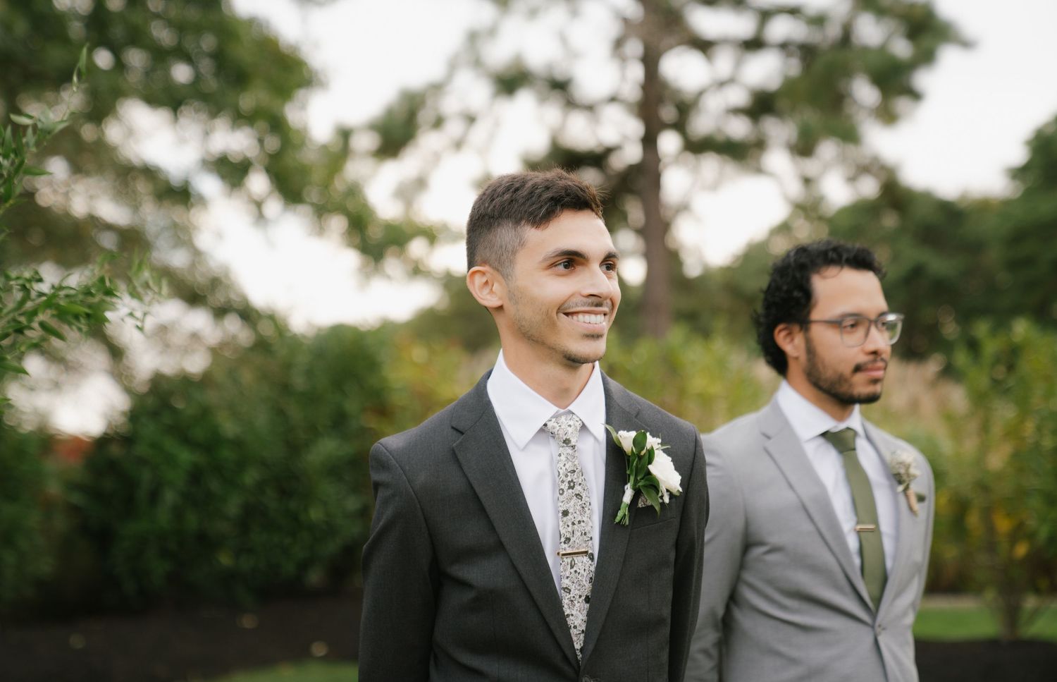 Groomsmen in gray suits and floral ties pose together outdoors during a wedding photoshoot.