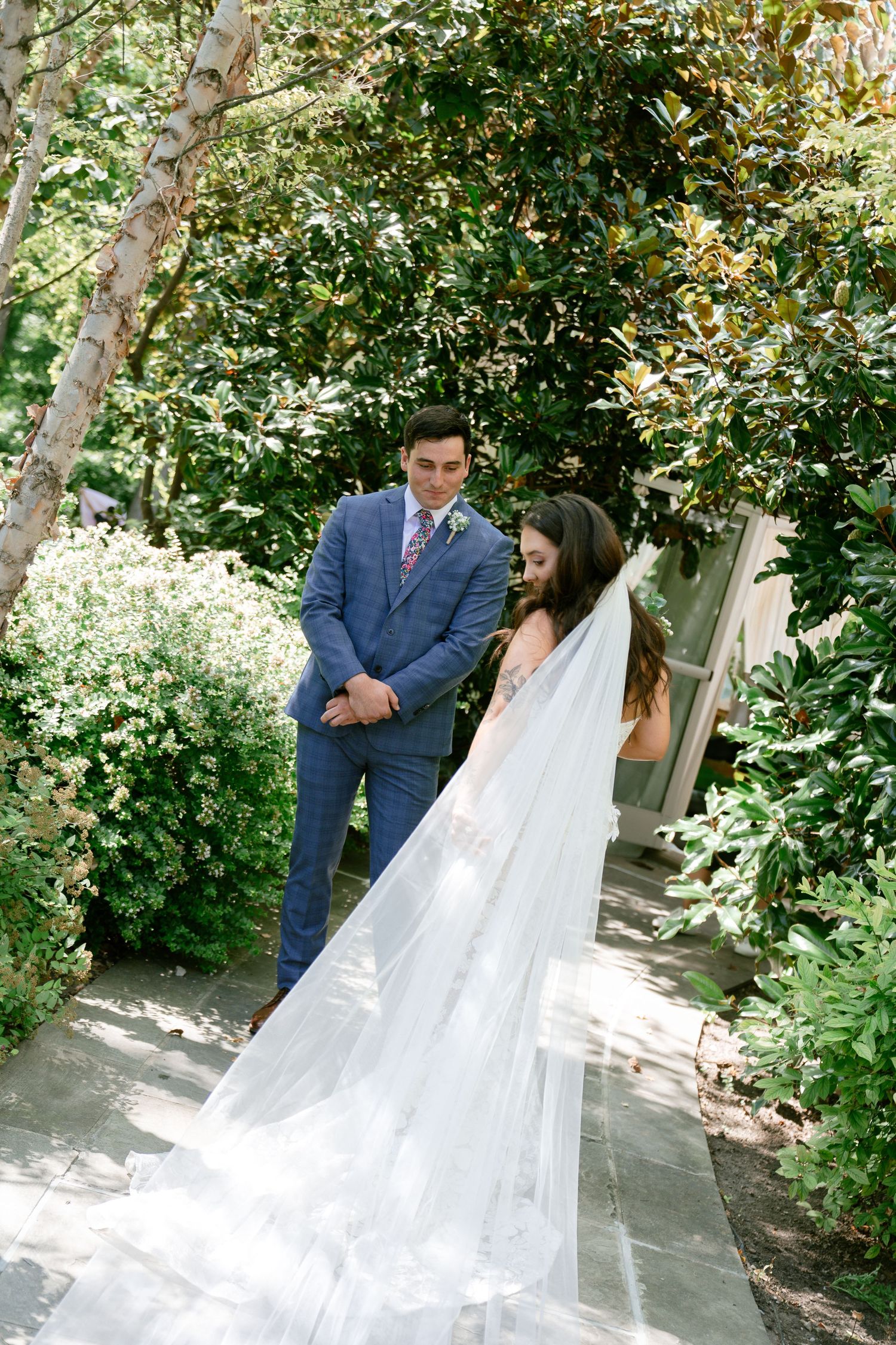 First look moment between couple in a lush garden setting with flowing white veil.