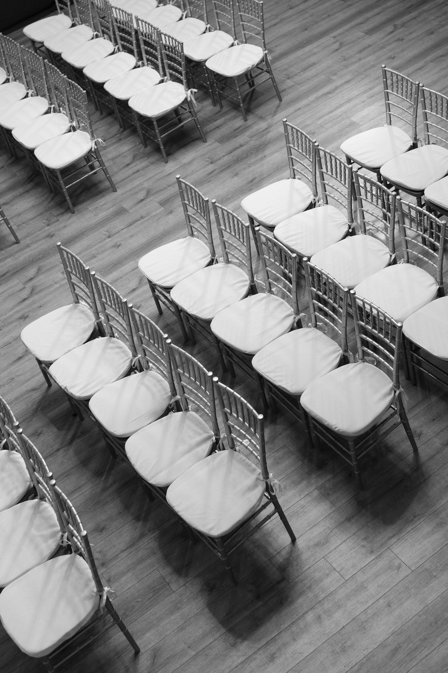 Rows of empty white cushioned chairs arranged in a formal seating layout on a wooden floor.