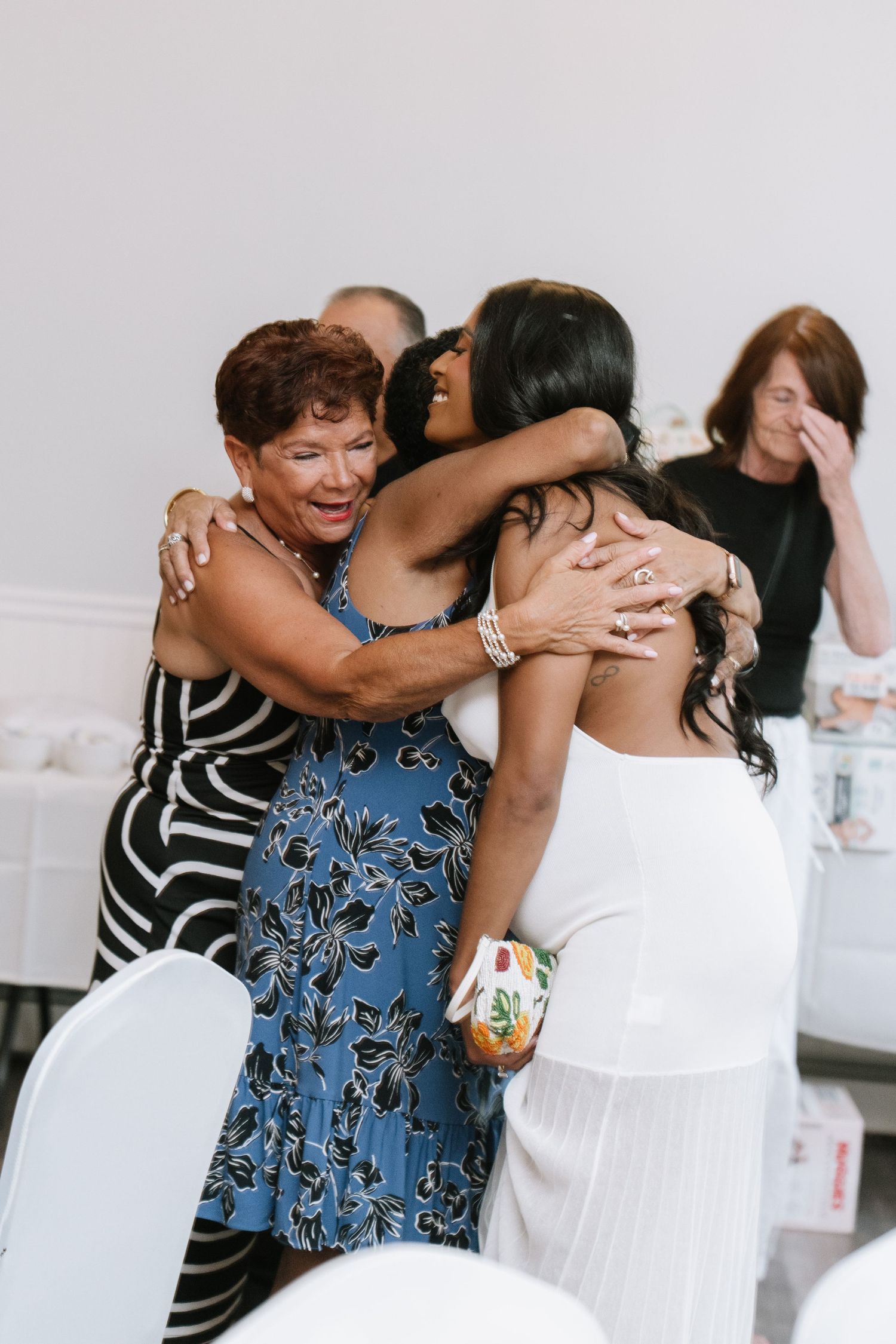 Joyful celebration with guests hugging and laughing at a white-themed party.