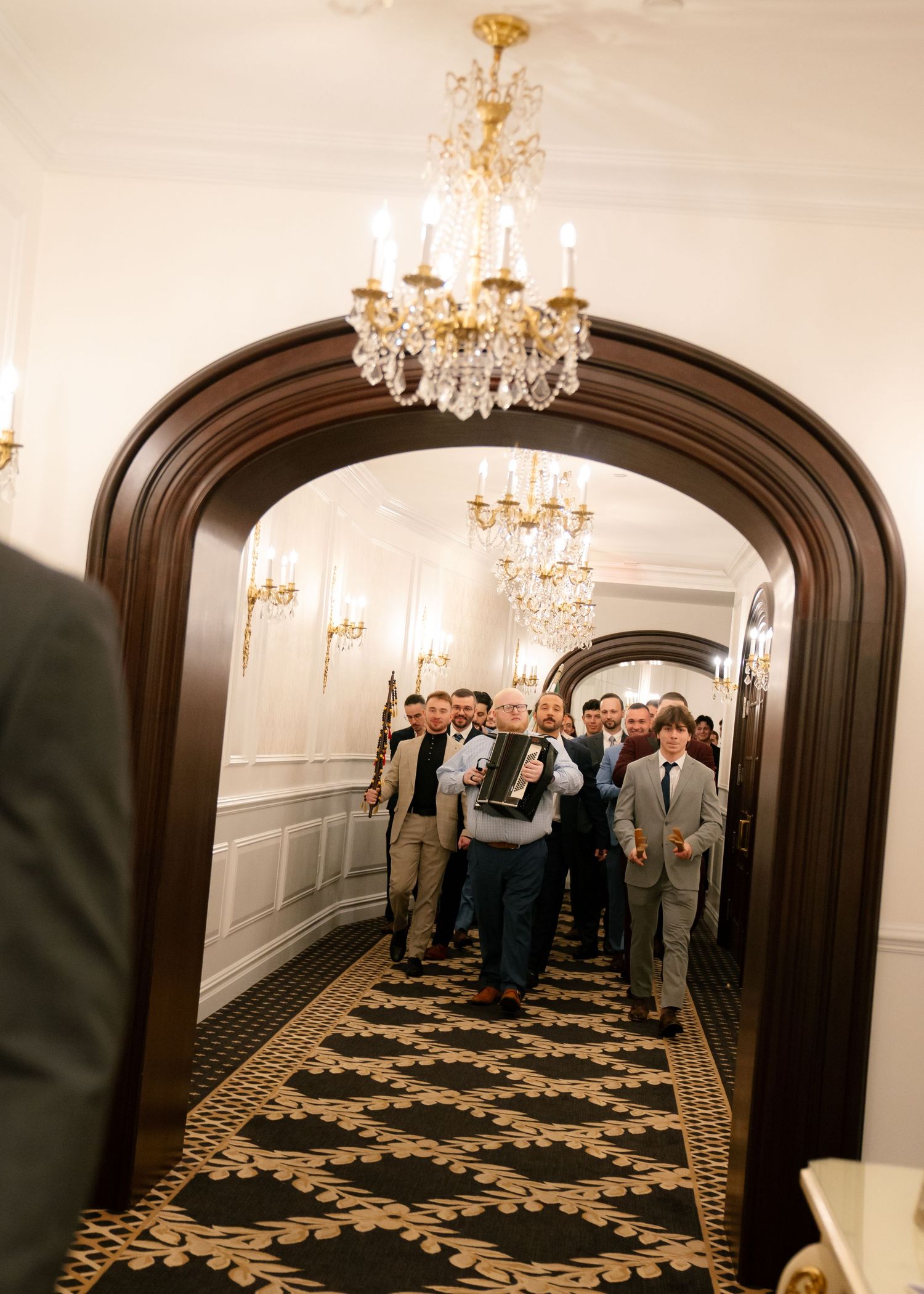 Wedding guests walking through an elegant hallway with crystal chandeliers and ornate archways.