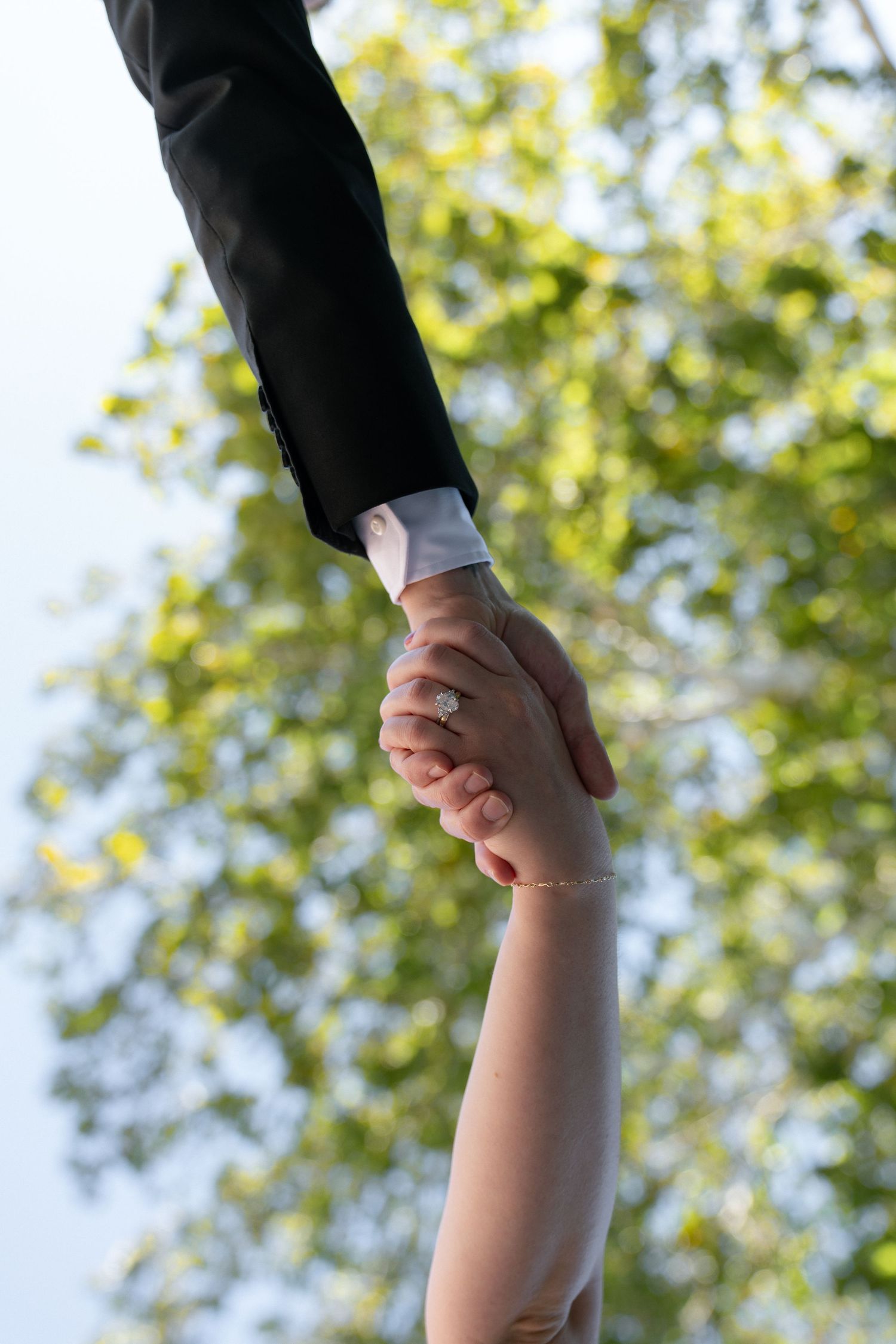 A series of hands holding each other in succession against a blurred green leafy background outdoors.