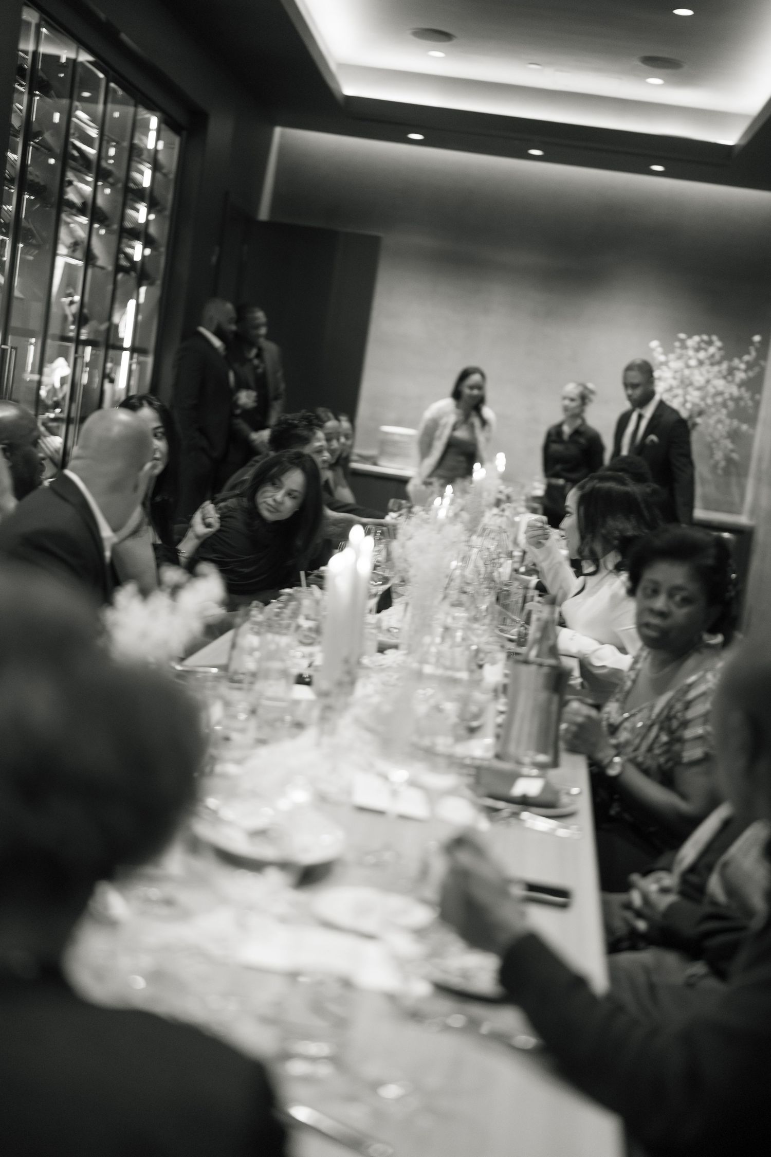 A black and white photo of wedding reception guests seated at elegantly decorated tables.