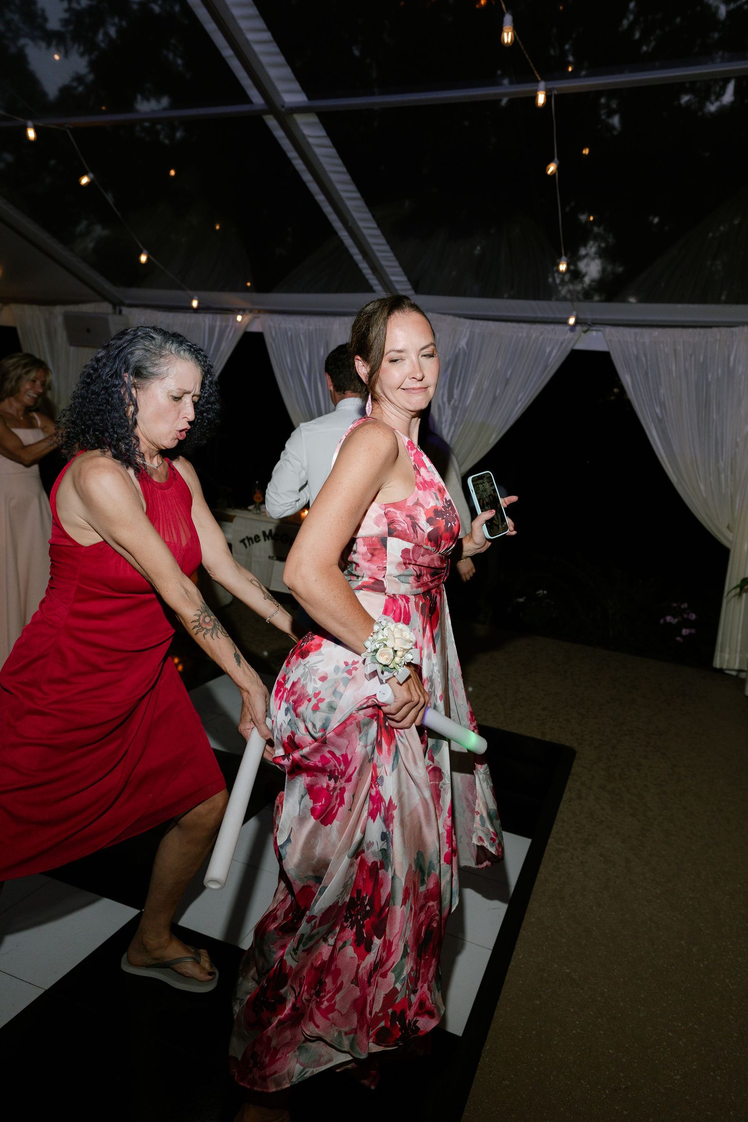 Wedding guests dancing on a black and white checkered floor, one wearing a vibrant red floral dress.